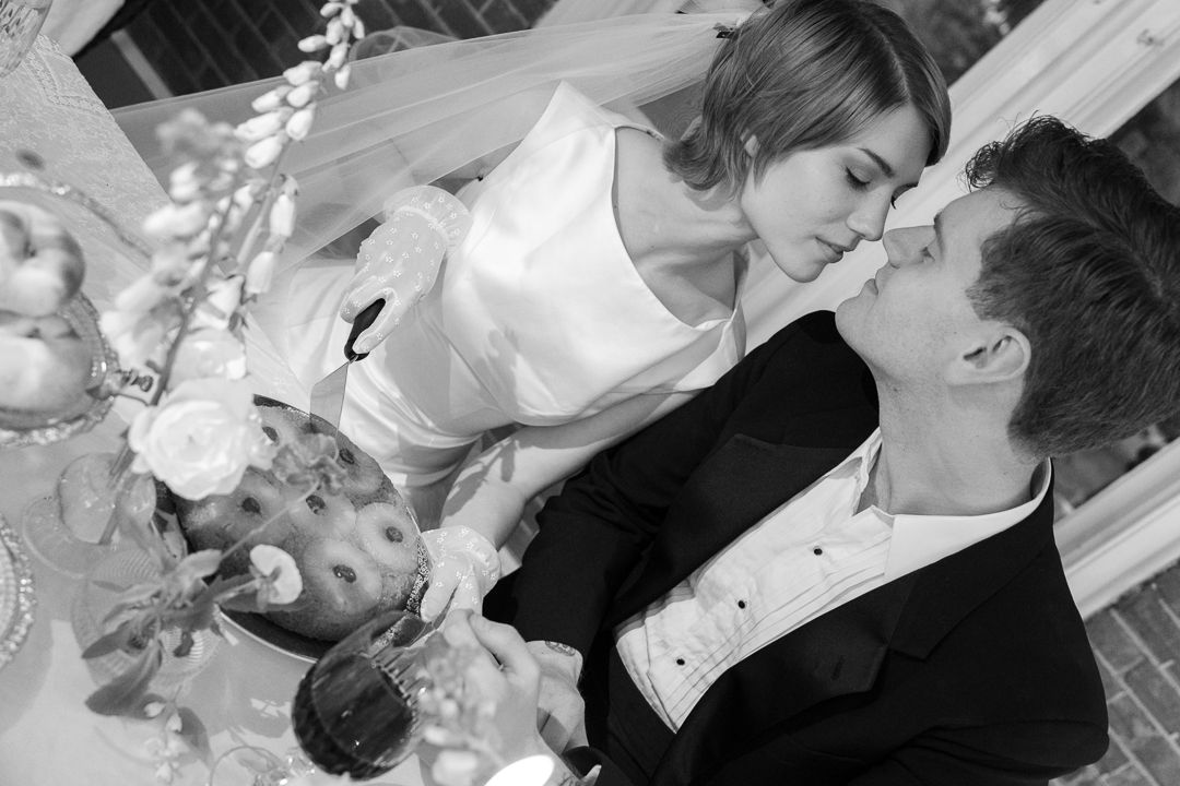 Black and white photo of bride and groom sharing a kiss while cutting their wedding cake.