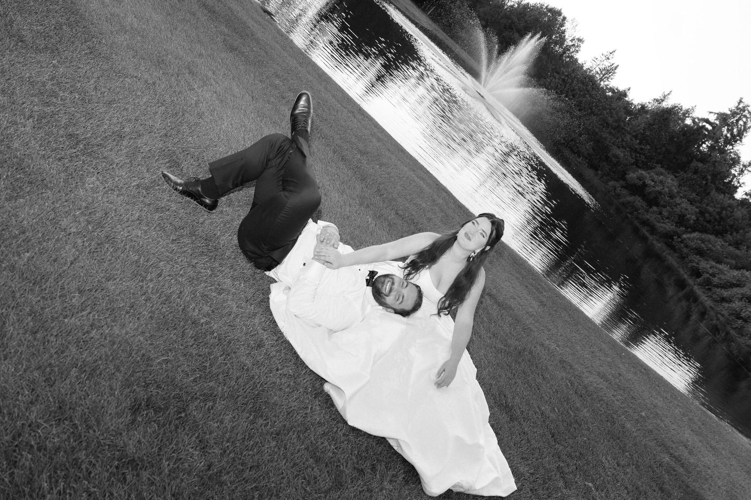 Black and white photo of a bride and groom dancing outdoors near a serene lake on their wedding day.