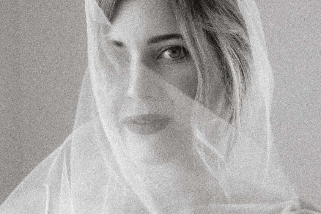 Close-up black and white portrait of woman draped in sheer white bridal veil.