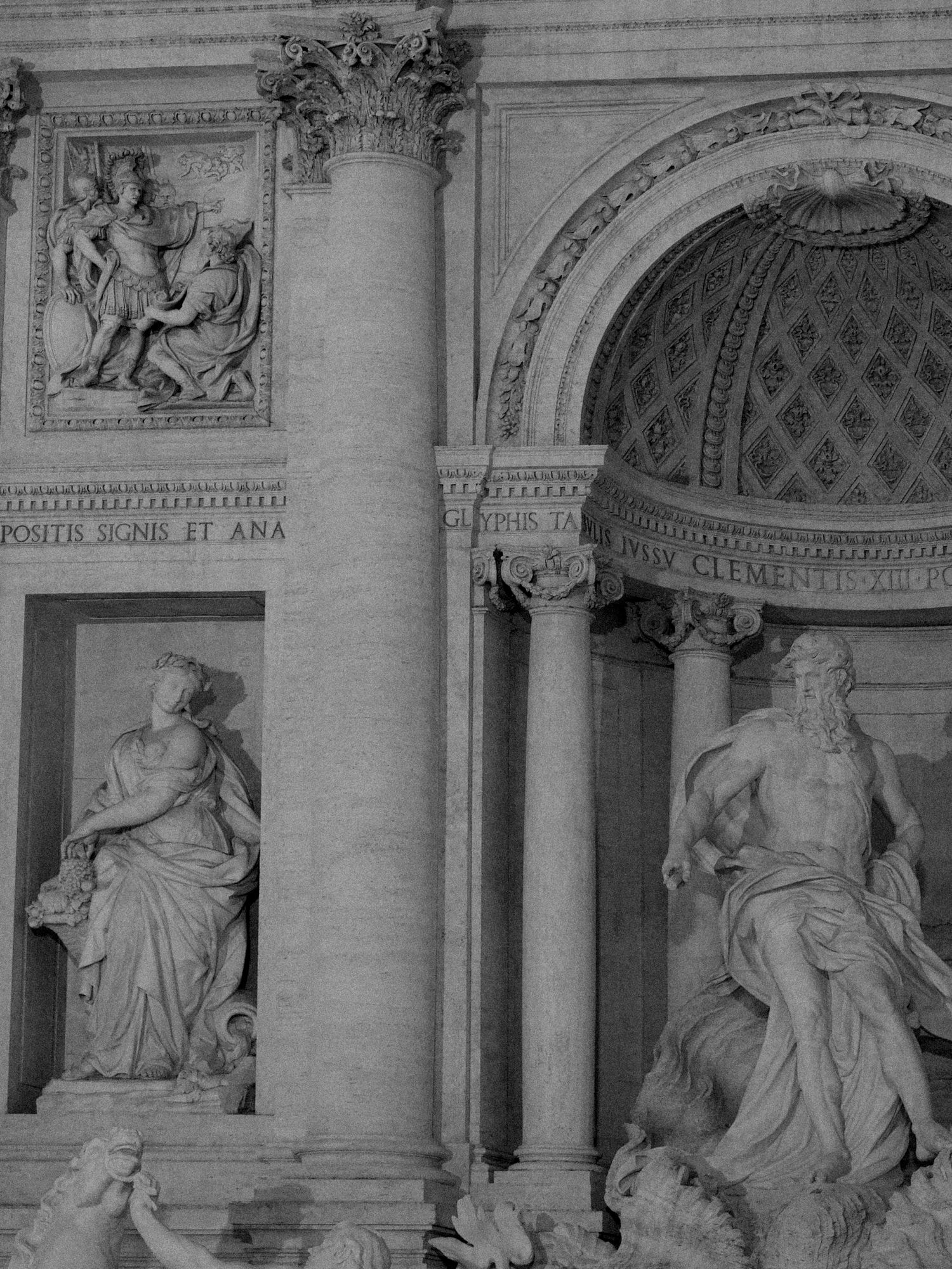 Black and white photo of ornate Trevi Fountain facade with classical statues and Roman architecture.