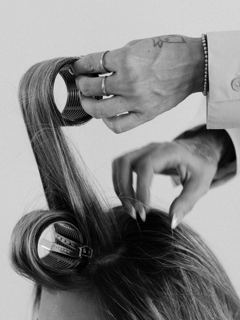 Hairstylist using round brushes to style long hair in black and white photo.