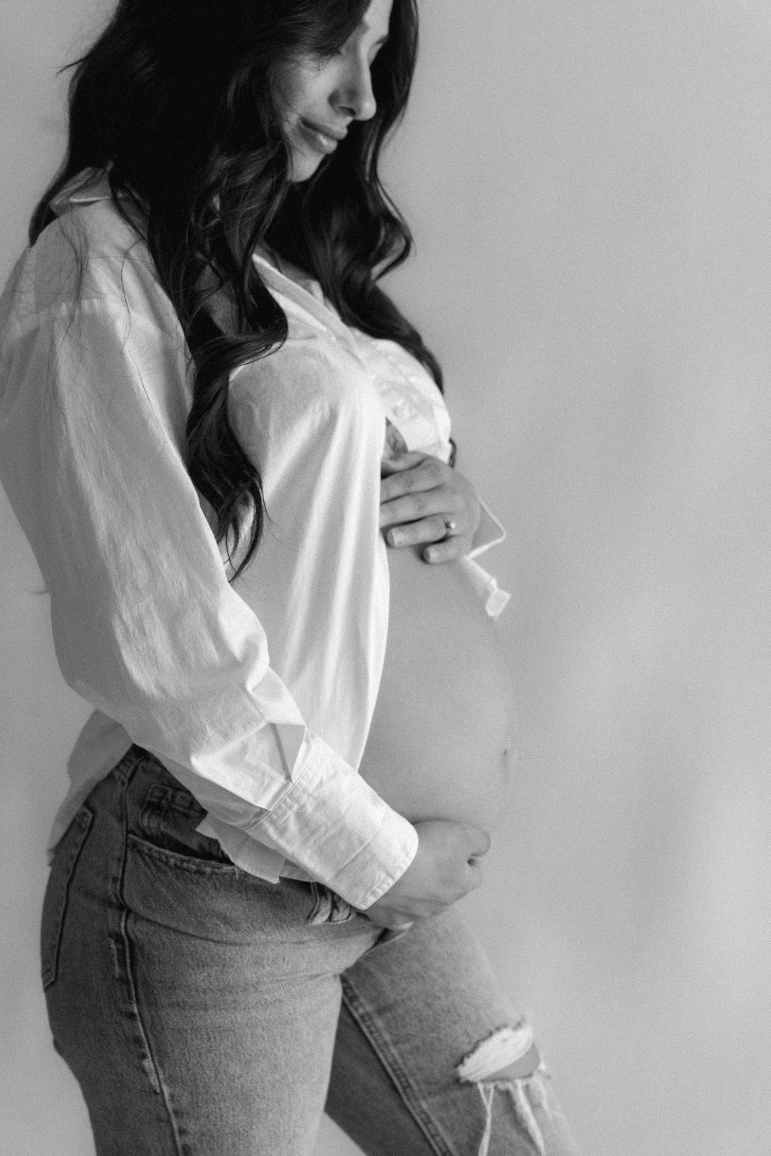 Black and white photo of a pregnant woman in white shirt and ripped jeans cradling her baby bump.