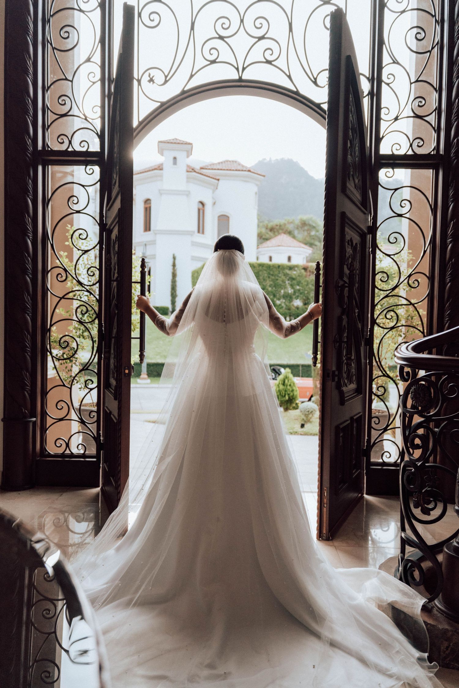 Novia caminando bajo arcos con luz suave / Bride walking through arched hall in soft light
Novia frente a puerta de madera antes de entrar