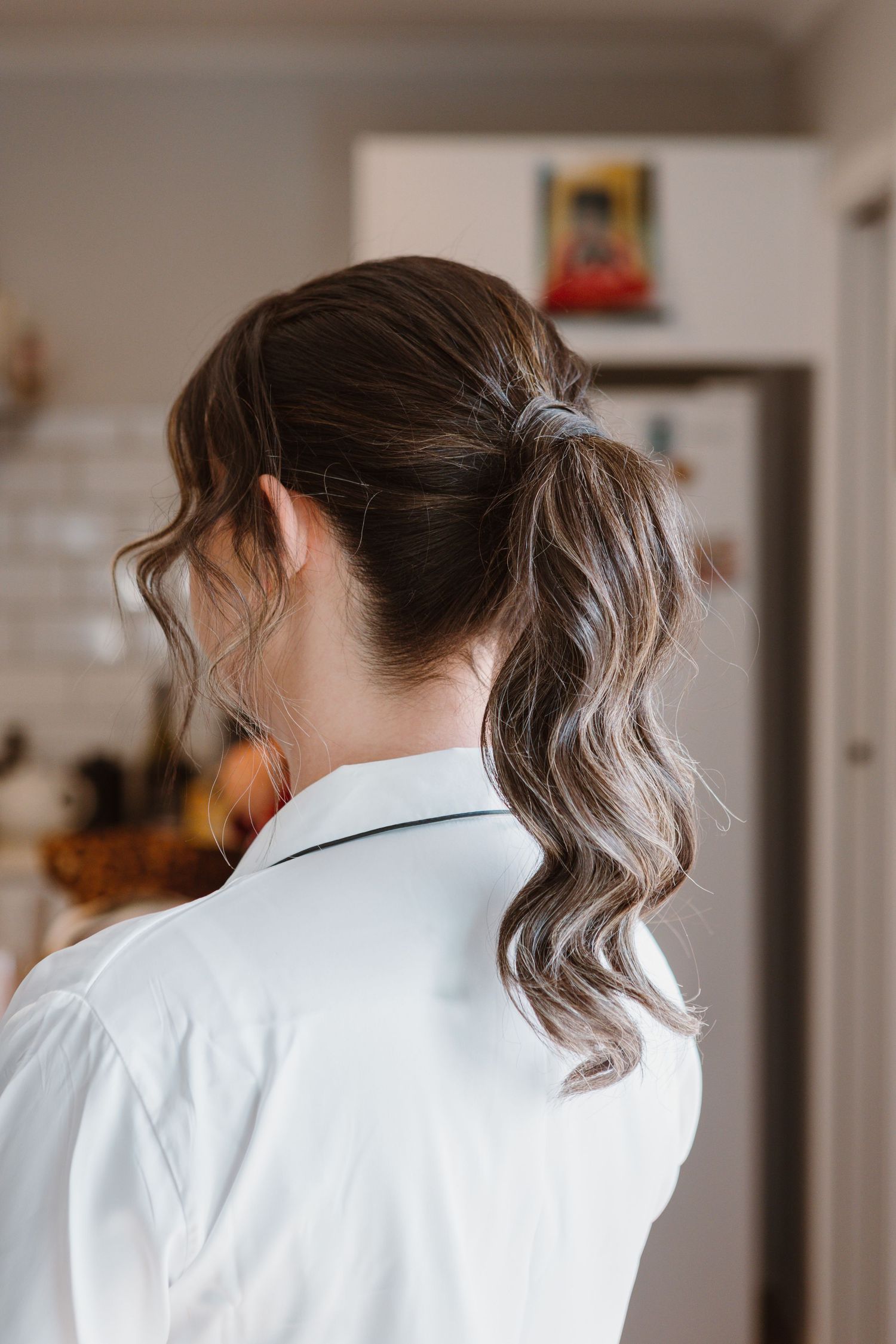 Woman with brown hair styled in ponytail shown from back view wearing crisp white collared shirt.