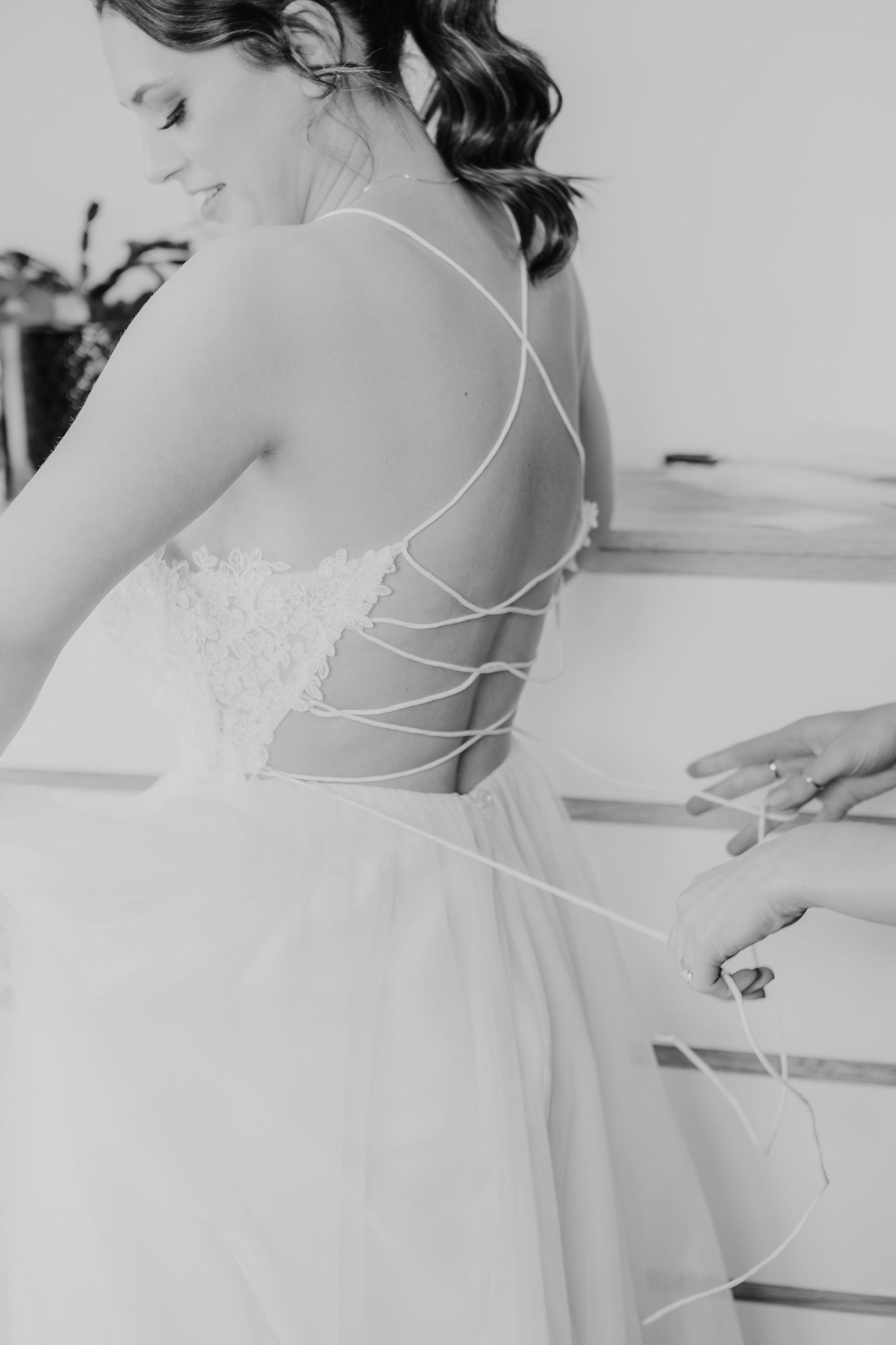 Close-up details of a white wedding dress showing delicate back straps and lace embellishments in a romantic style.