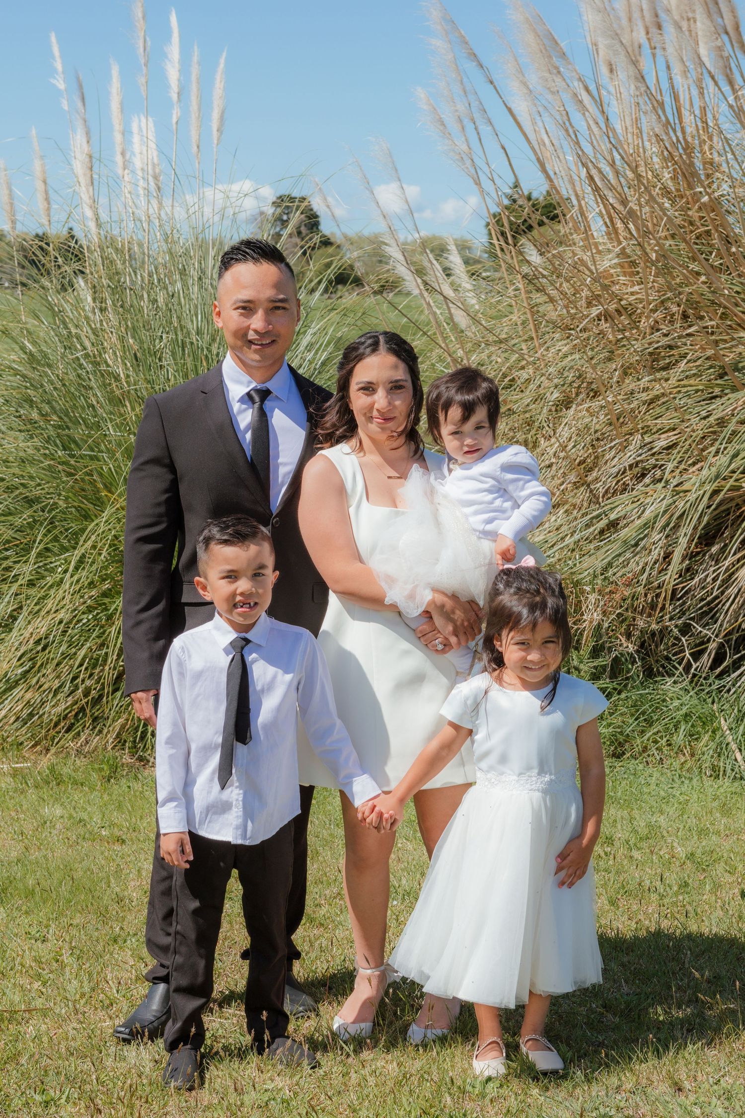 People in formal attire pose together on a grassy hill with tall beach grass in the background.
