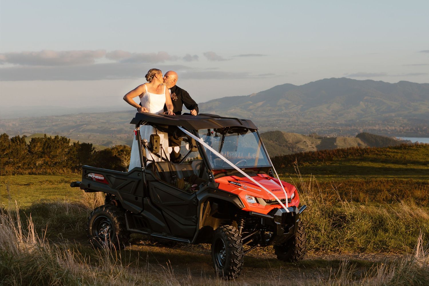Orange all-terrain vehicle on mountainous terrain during sunset creates striking silhouette against dramatic sky.