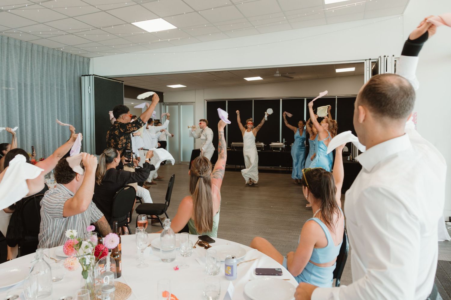Wedding guests celebrate by waving napkins in the air at a reception venue.