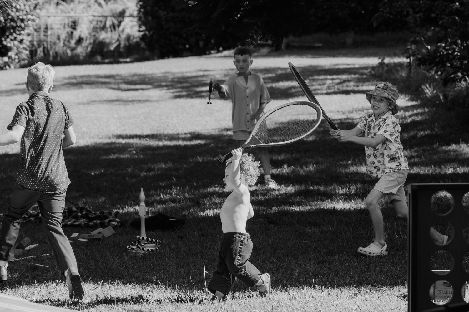 Children playing outdoors with a hula hoop in a sunny park, captured in black and white photography.