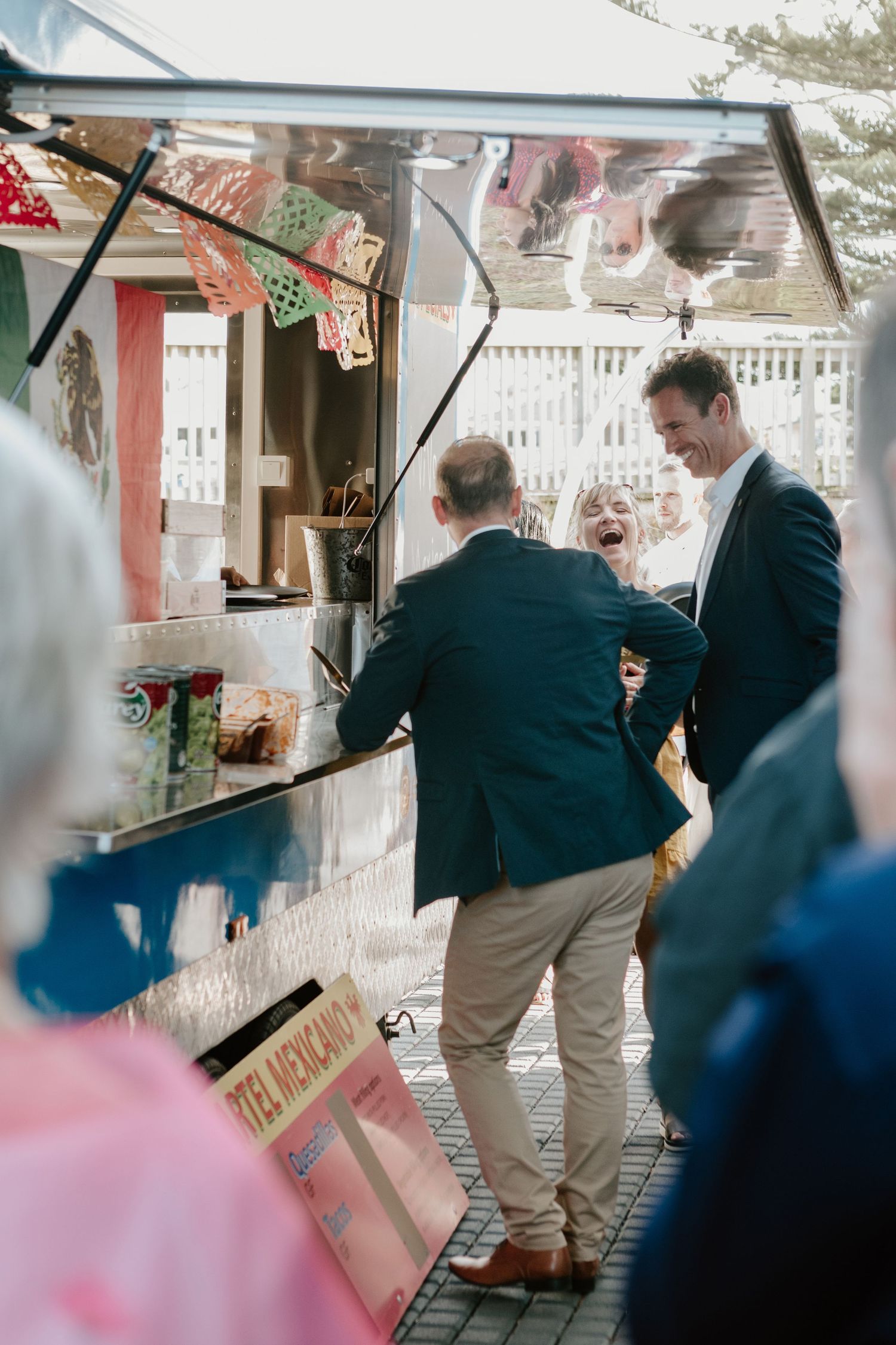 Two guests in dark suits stand at a decorated food vendor cart or kiosk at an outdoor event.