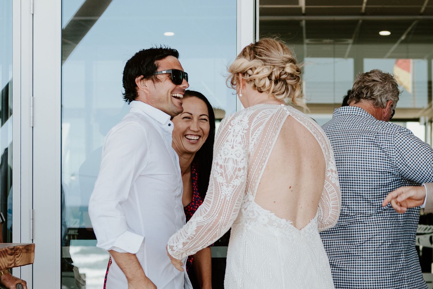 Wedding guests celebrating in a bright indoor venue with large windows. Papamoa Surf Lifesaving Club Wedding