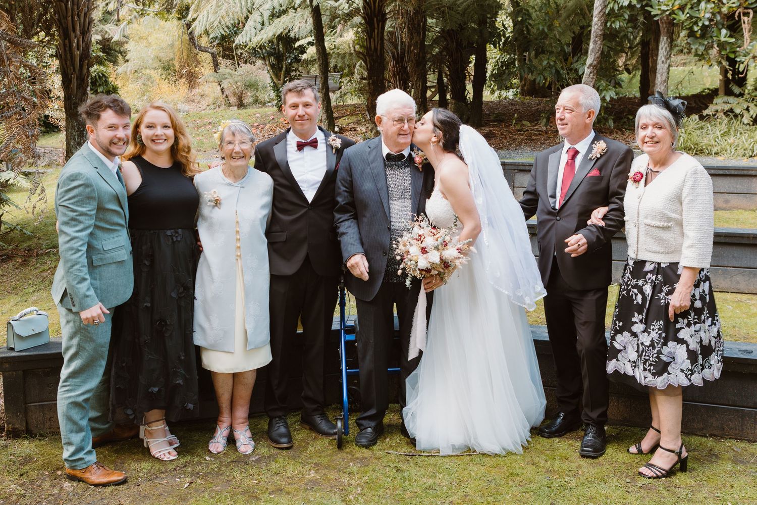 Extended family wedding portrait in garden with mix of formal attire.
