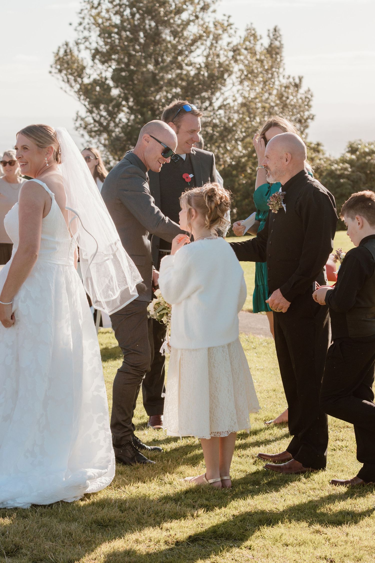 Guests mingle and dance together during an outdoor wedding reception on a sunny grassy lawn.