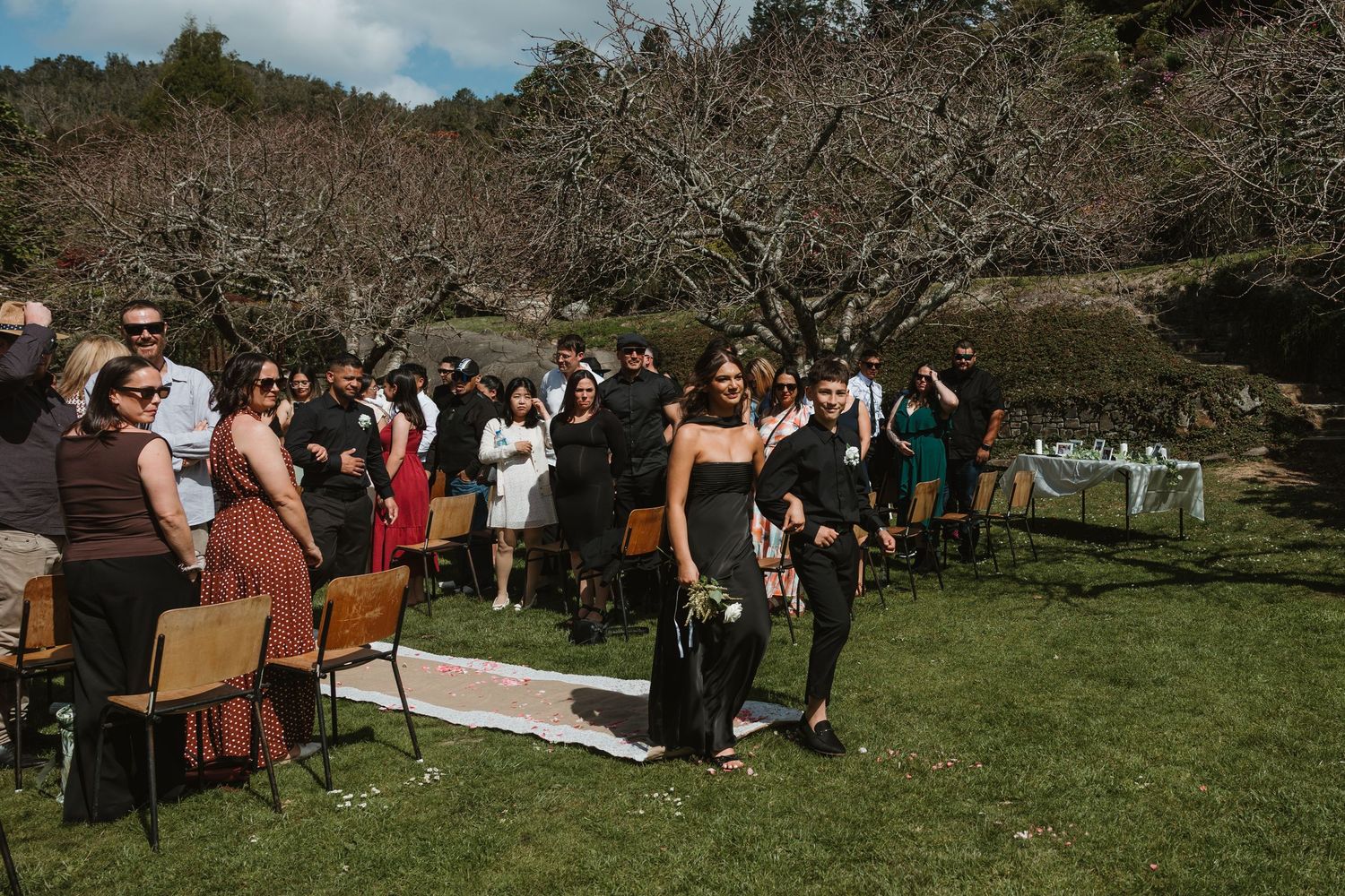 Outdoor wedding ceremony setup with wooden chairs arranged in rows on a grassy hillside under blue skies.