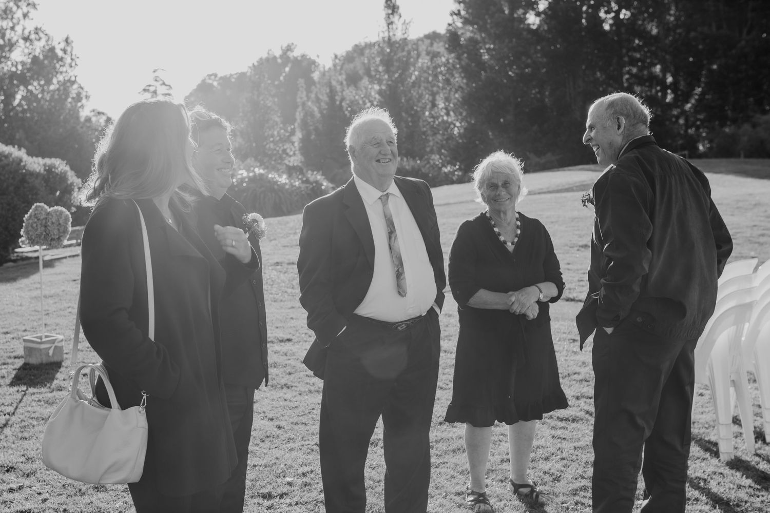 People in formal black attire walk on grass in a single line during what appears to be an outdoor ceremony.