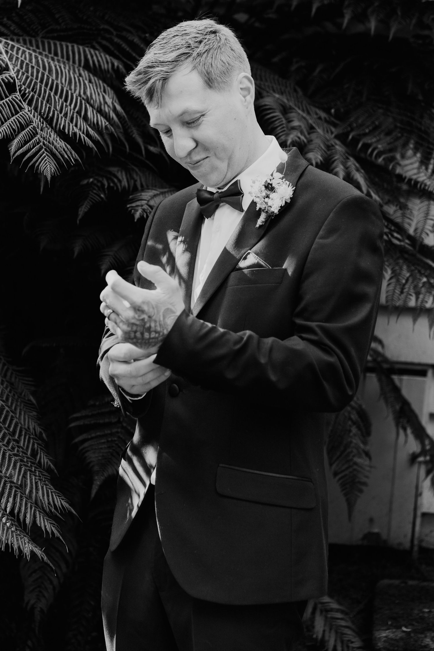 Someone wearing a black tuxedo looks down at their phone during what appears to be a formal event.