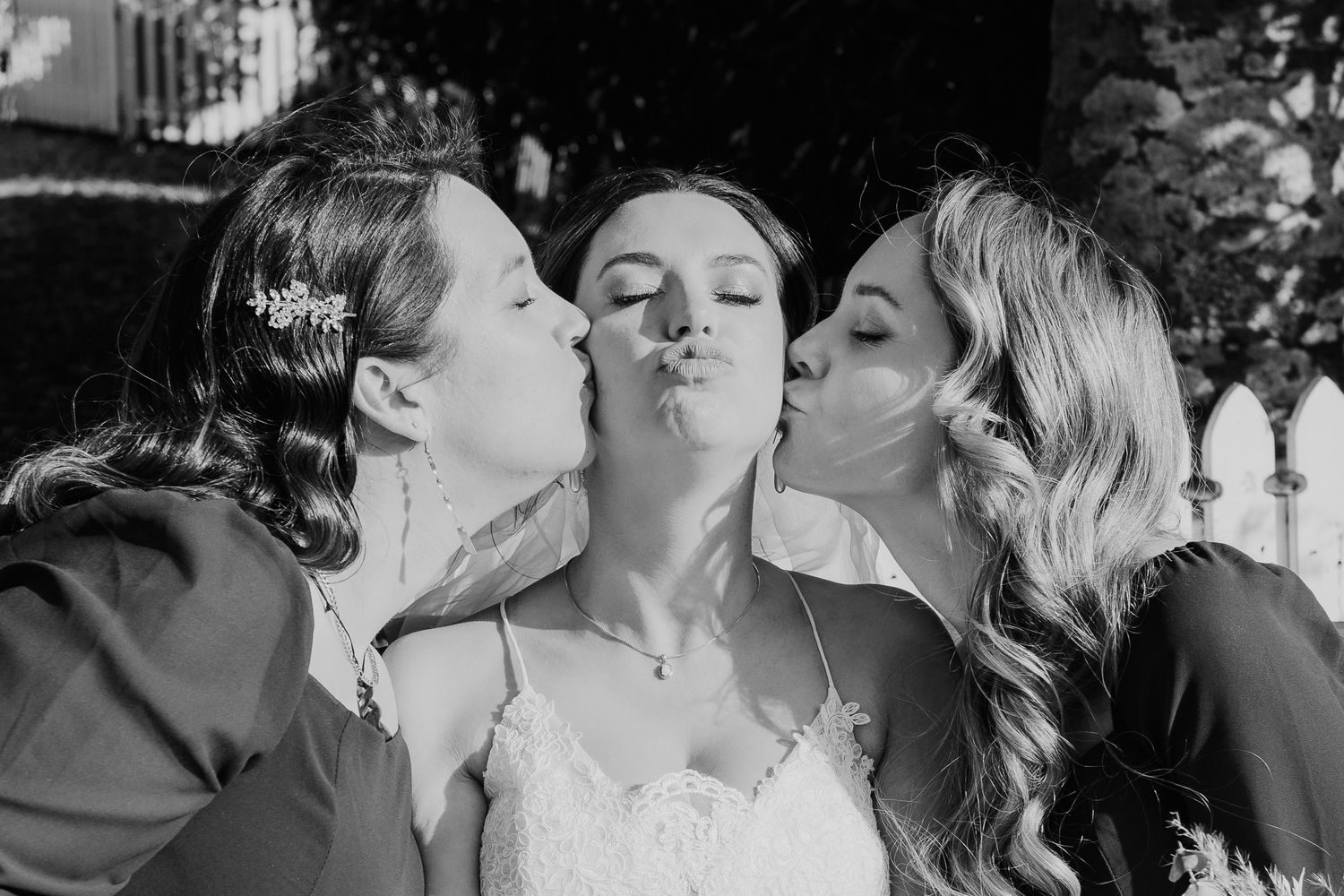 Three women in wedding attire share a playful kiss pose for a black and white photo.