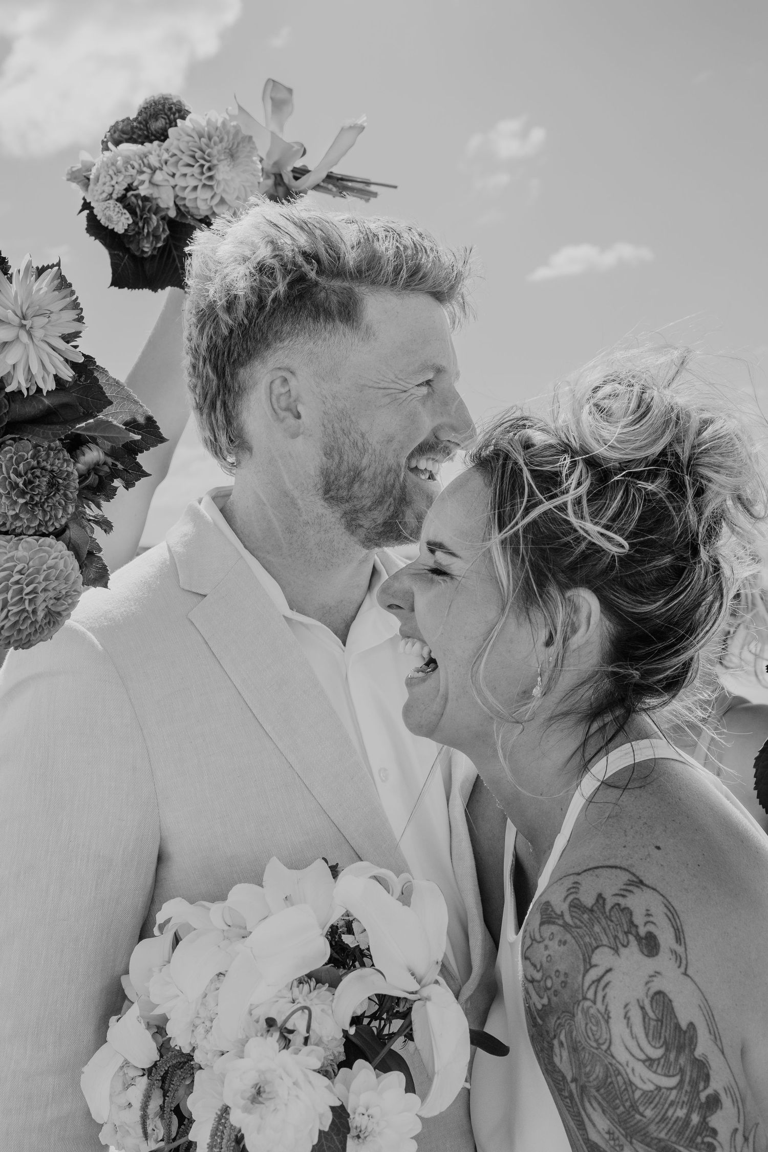 Black and white photo of a laughing bride and groom sharing a joyful moment at their outdoor wedding ceremony.