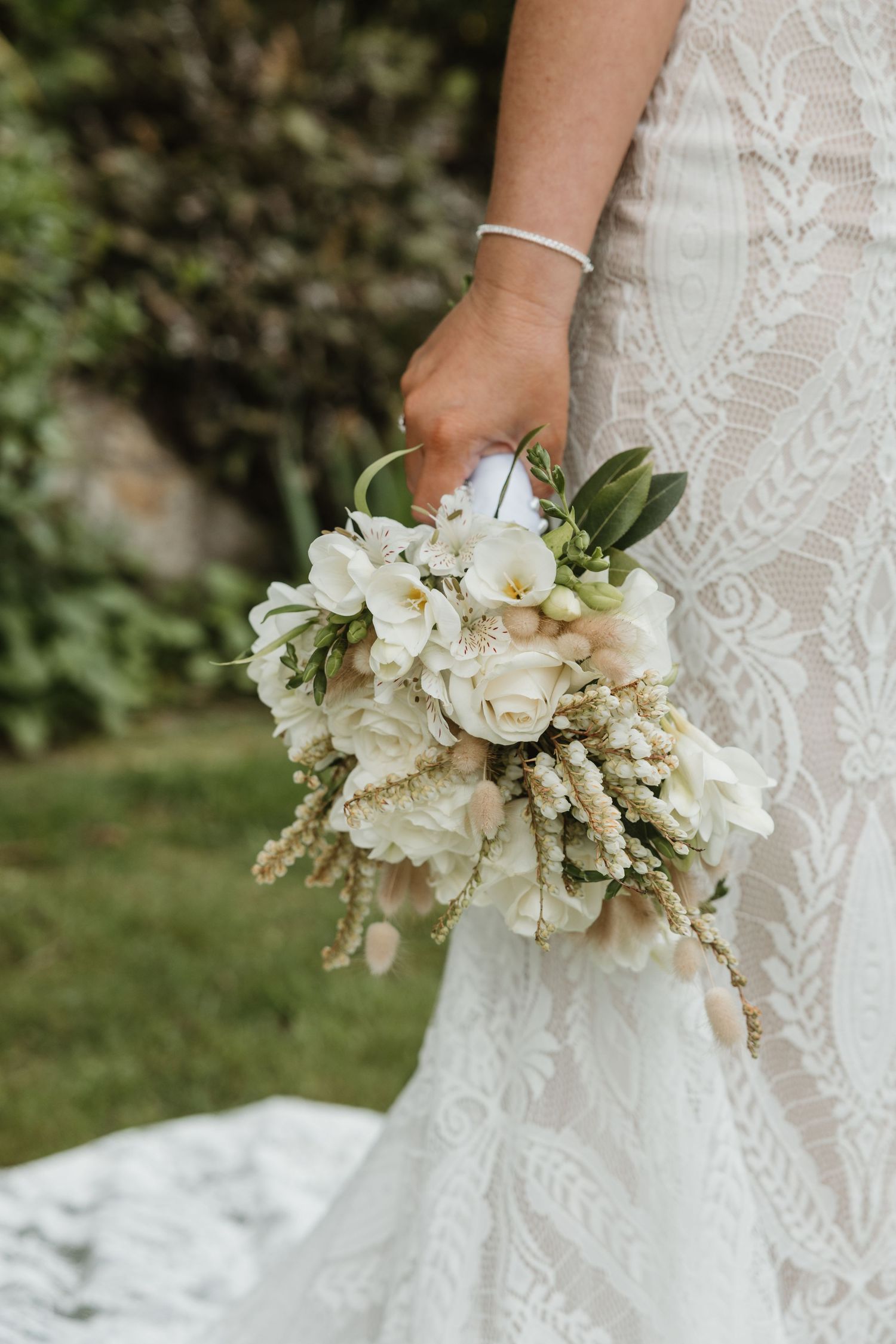A white bridal bouquet with roses, orchids and delicate dried elements shown from different angles against a garden backdrop.