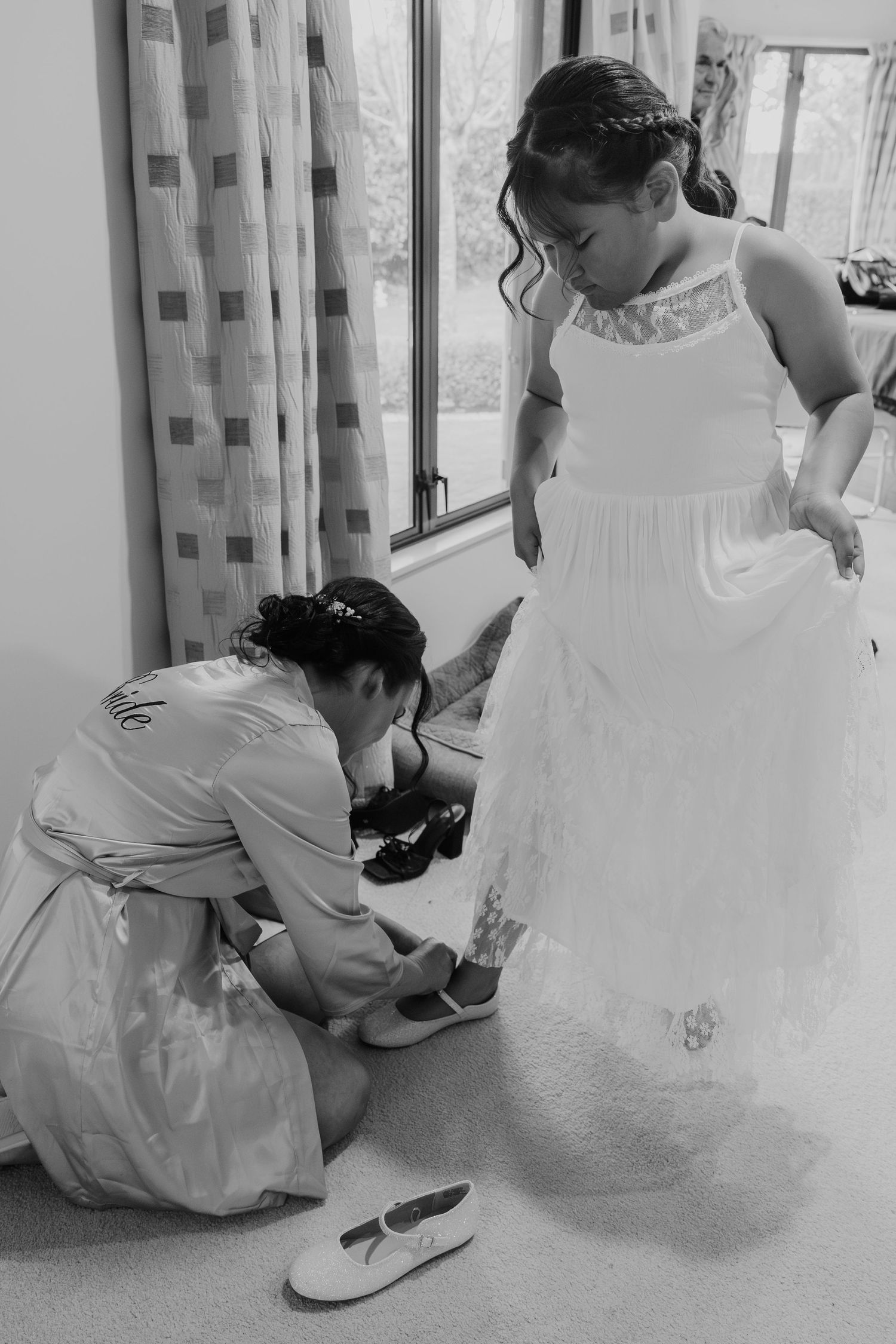 A series of black and white photos showing someone helping to adjust a formal white dress and shoes.