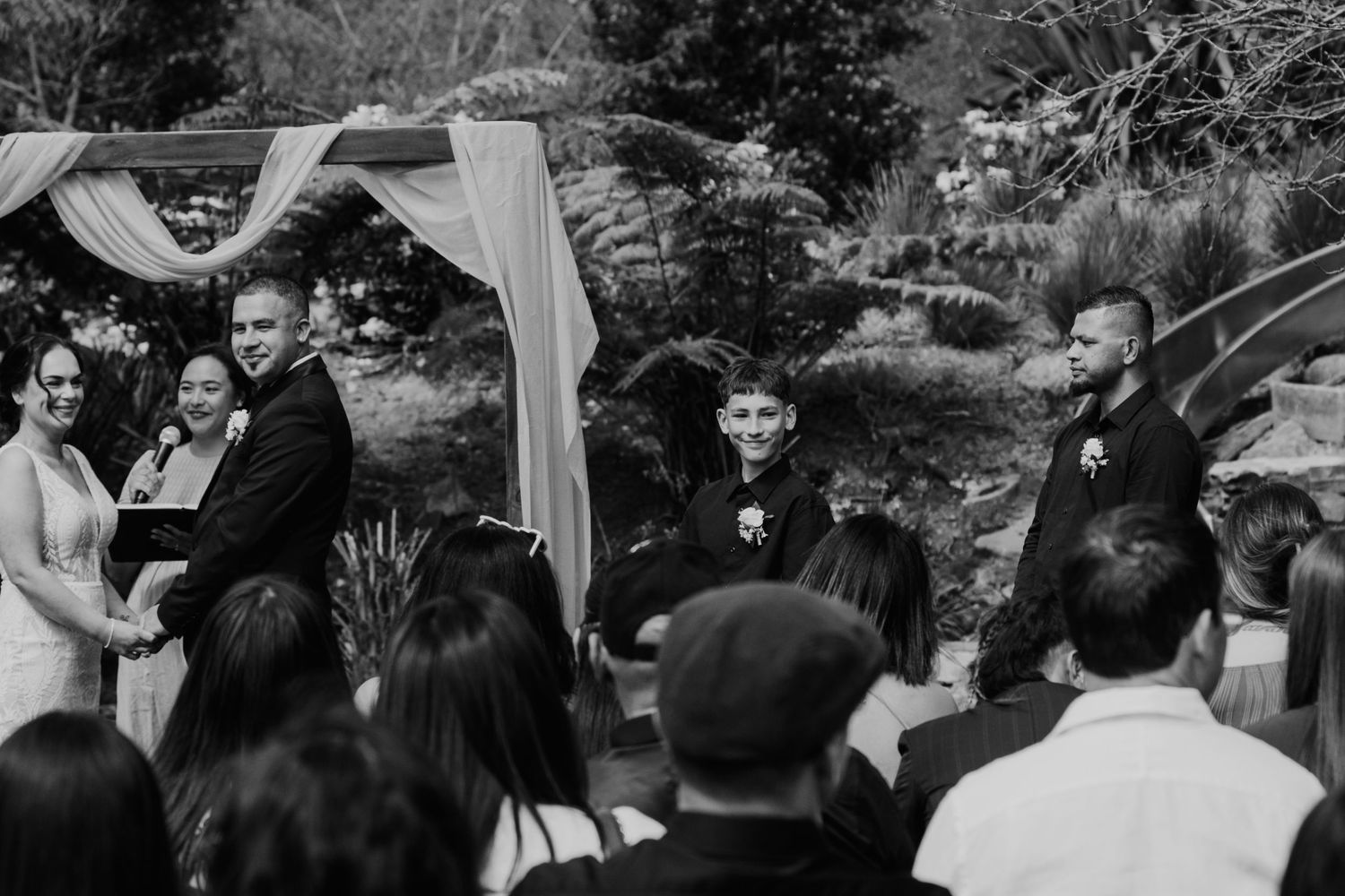 Wedding guests gather under white canopies during an outdoor garden ceremony celebration.