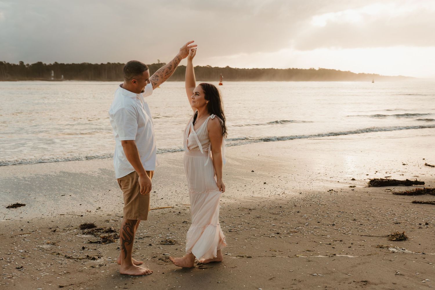 Couple walking together on a sandy beach at sunset with warm golden light reflecting off the ocean.