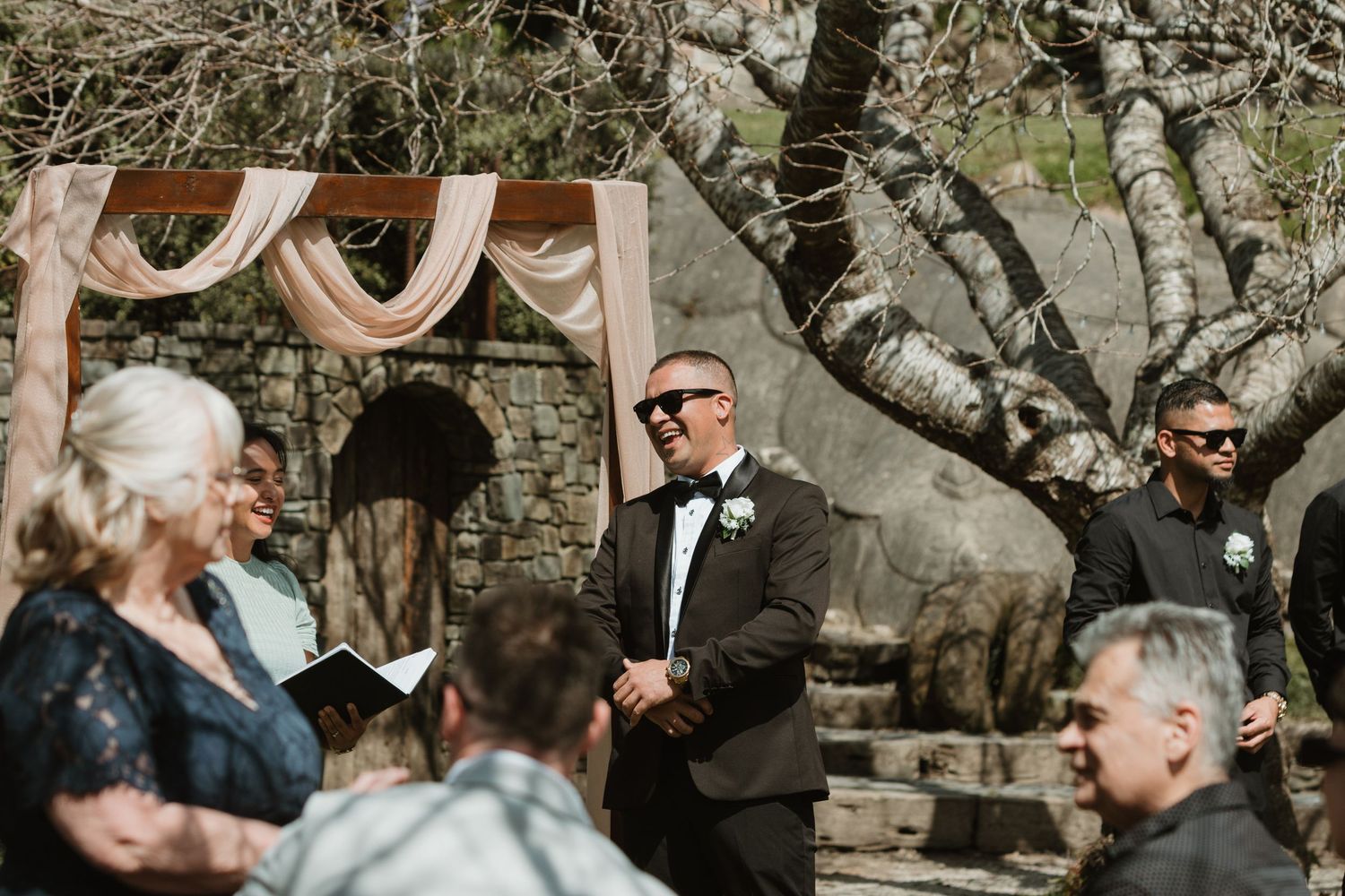 A couple shares a joyful moment during their outdoor wedding ceremony surrounded by natural stone walls.