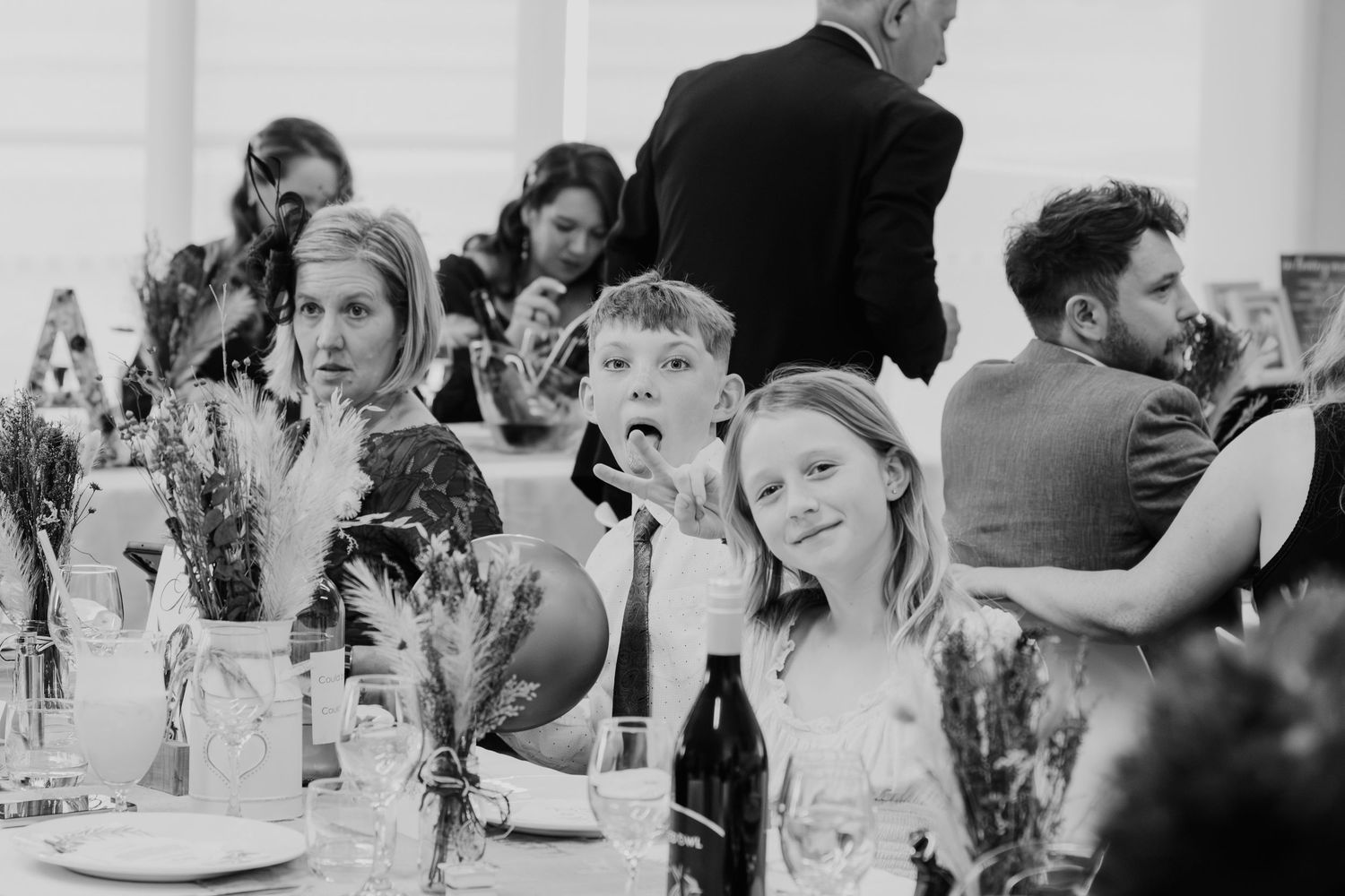 Black and white wedding reception scene with decorated tables and guests mingling indoors.