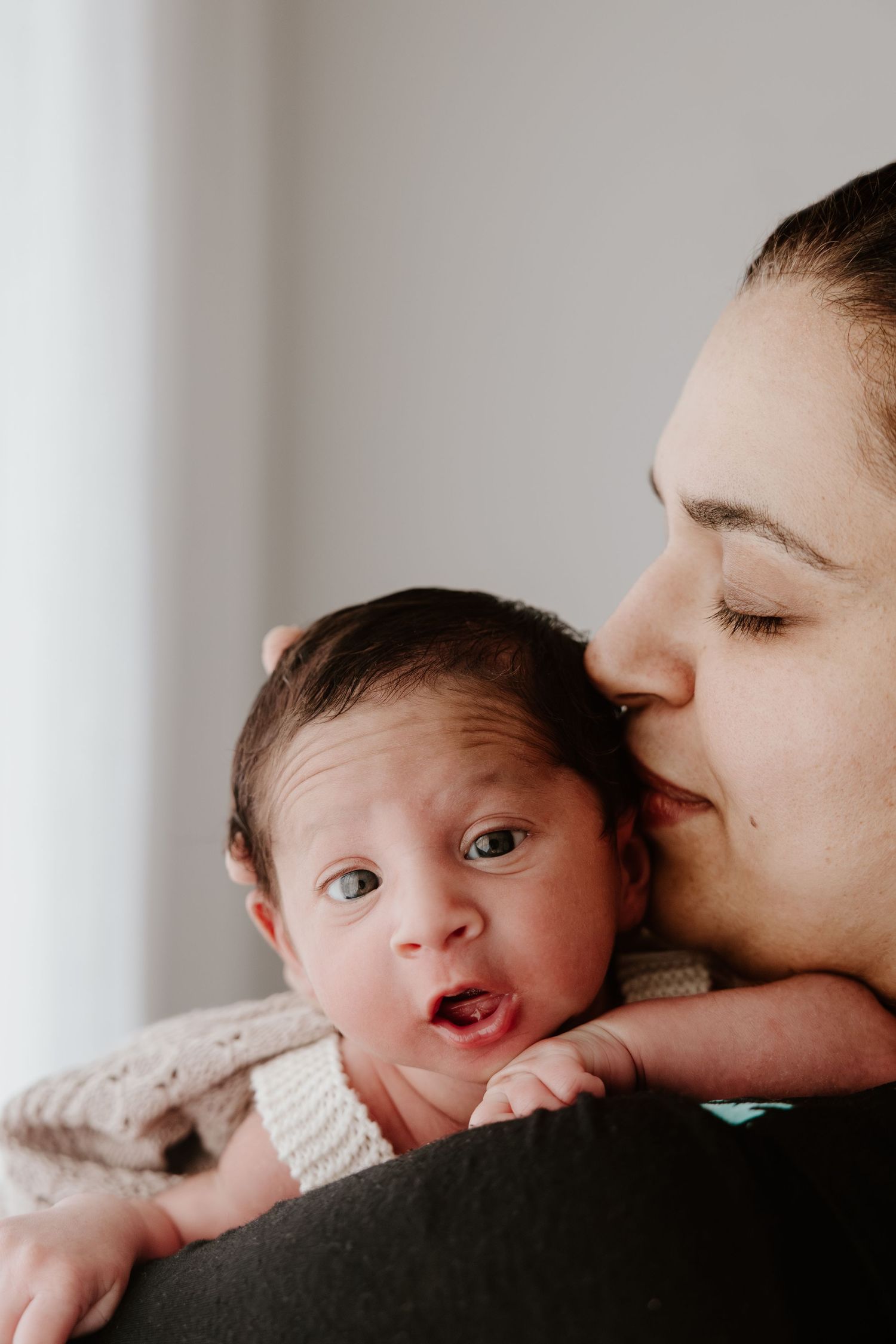 A tender moment showing a parent kissing a baby, who is giving an adorable expression. Newborn photography Tauranga