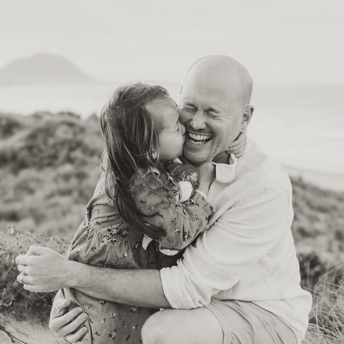 A couple embraces and laughs together during an outdoor photoshoot in a desert landscape setting.