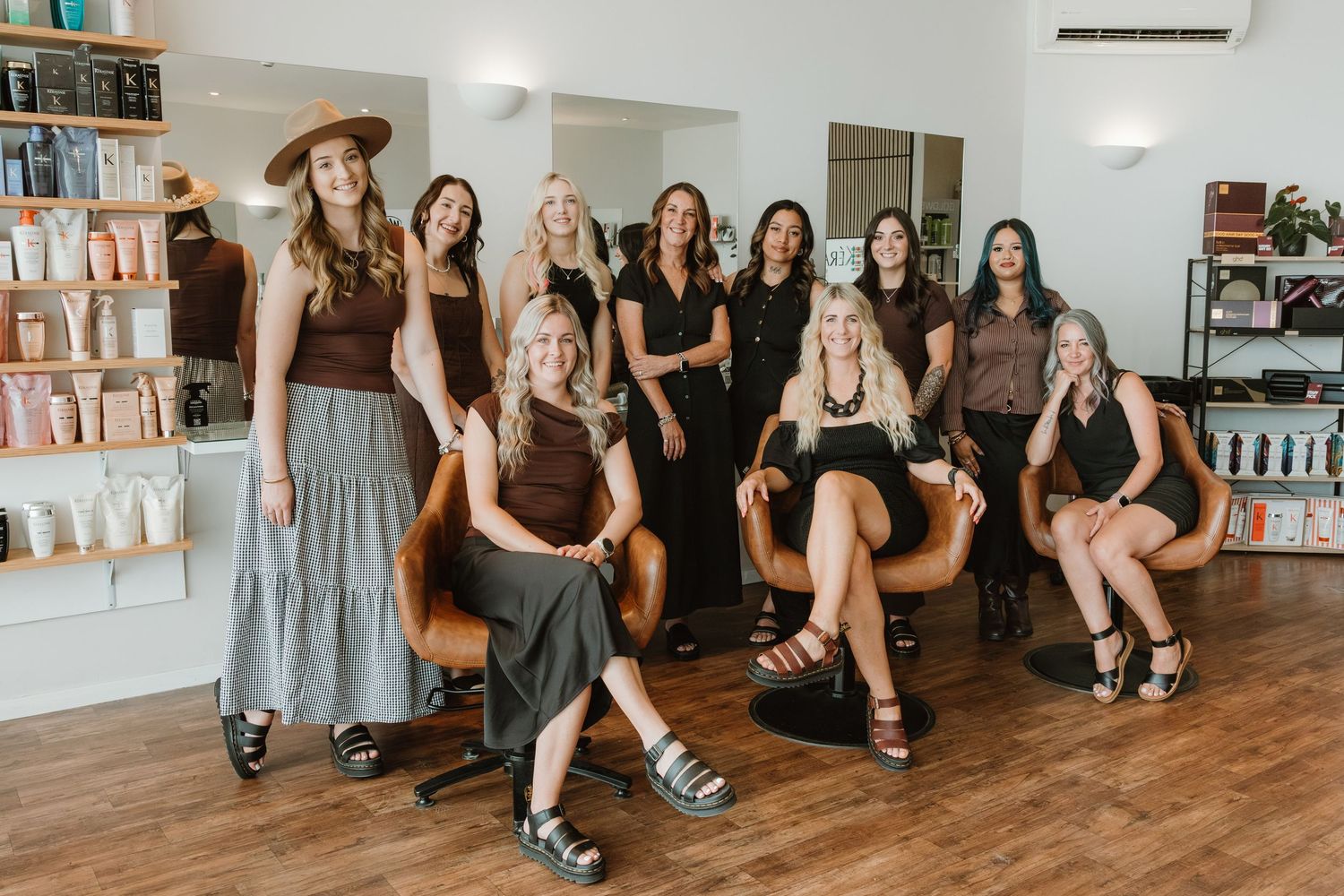 A group of people sitting on wooden floors in a studio space wearing casual attire and smiling together.