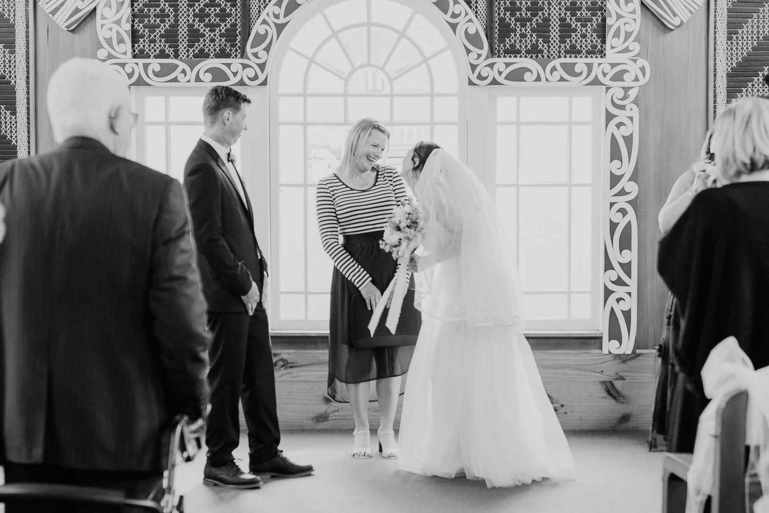 Wedding party members in formal attire gather inside an elegant ballroom with ornate decor and arched windows.