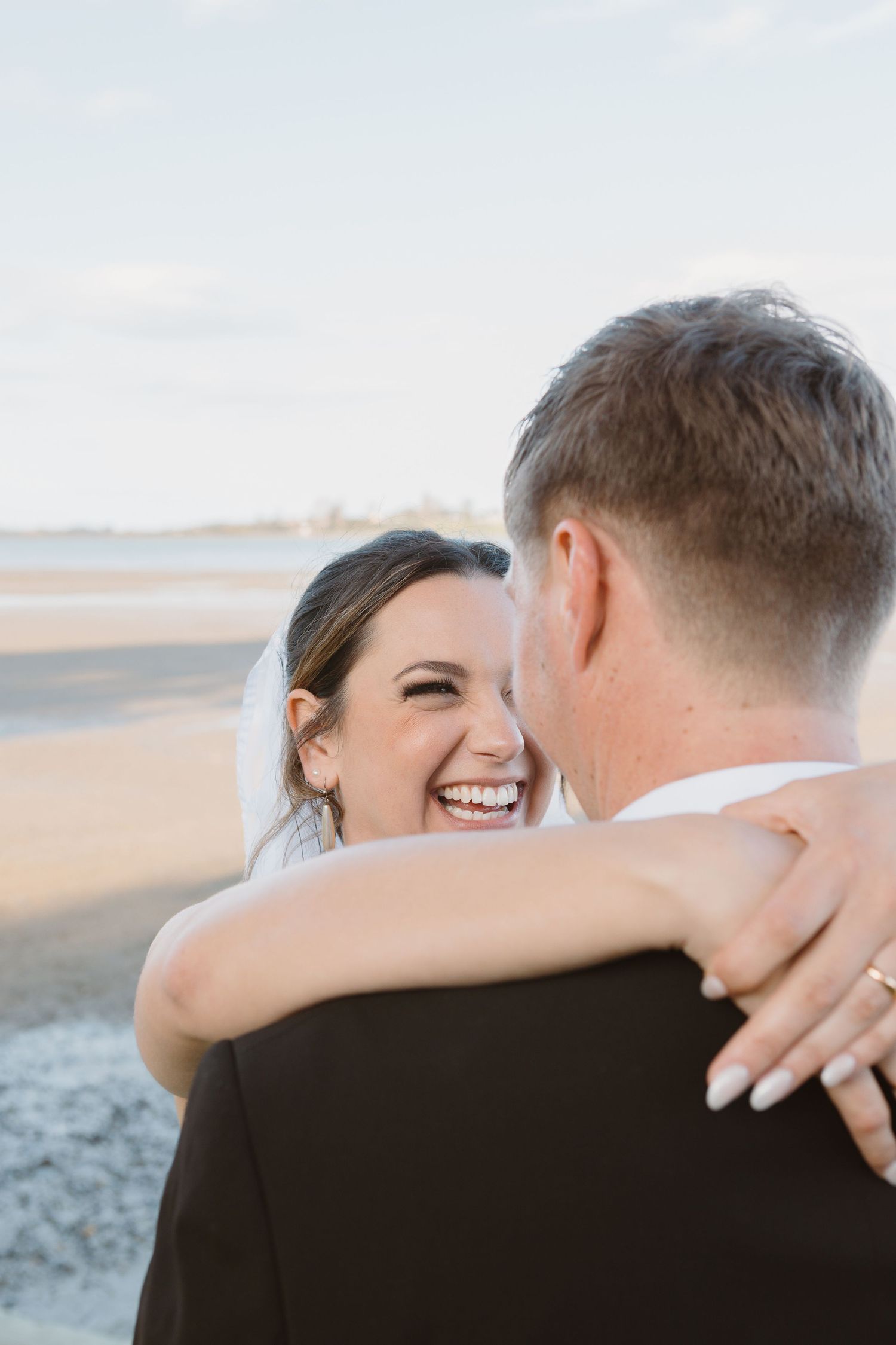 A romantic couple shares joyful embraces and laughter while standing together on a scenic beach at sunset.