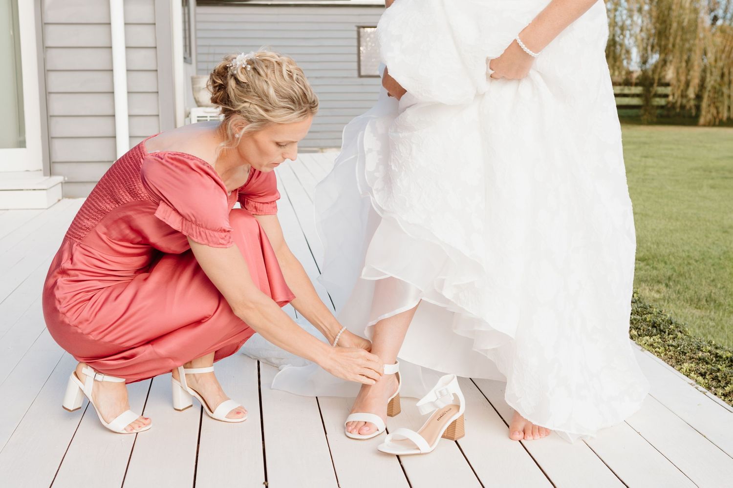 Young child in a coral dress reaches down to pet a white fluffy rabbit on a porch while wearing a bow headband.