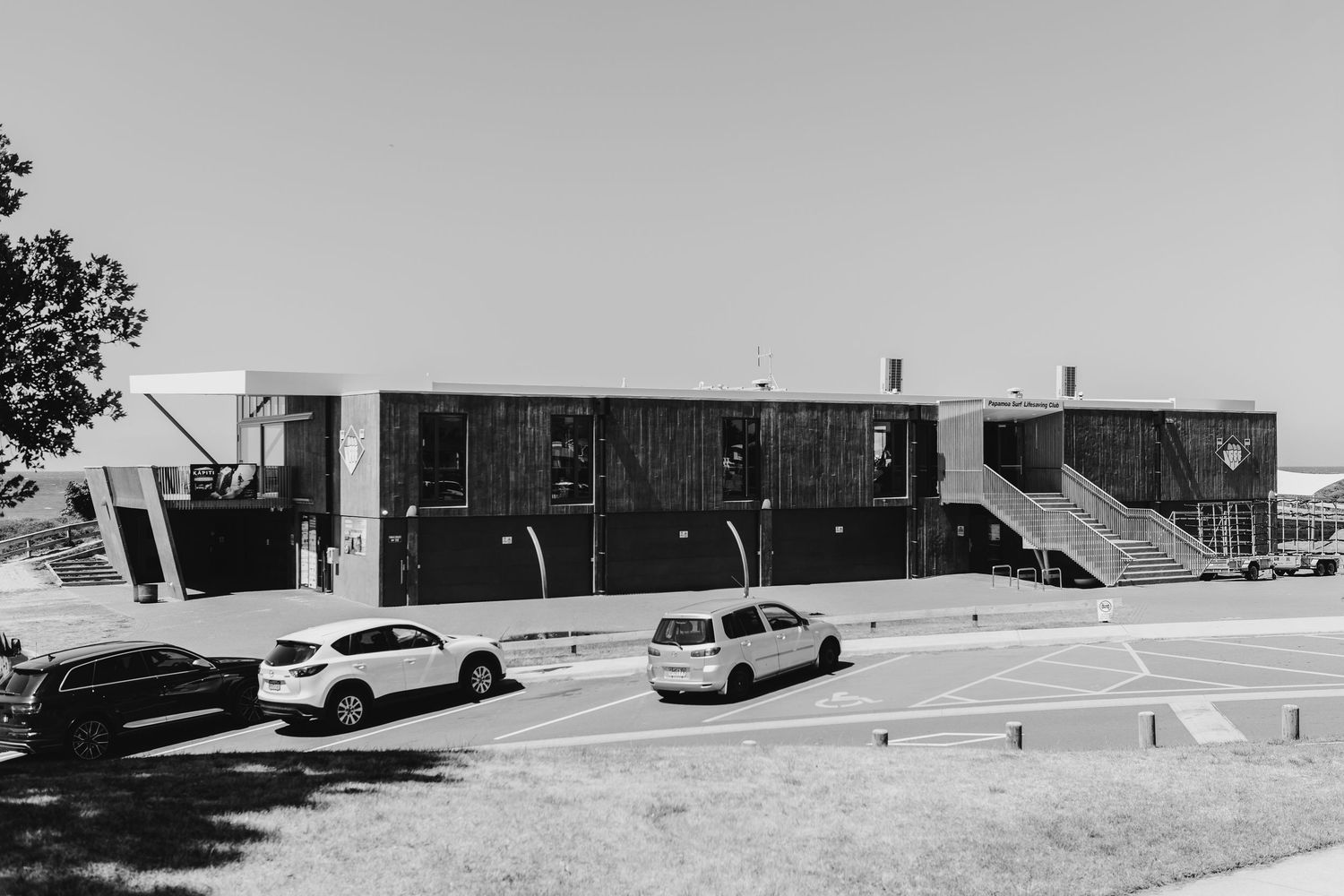 Vintage black and white photo series showing exterior views of a mid-century modern commercial building and parked cars.