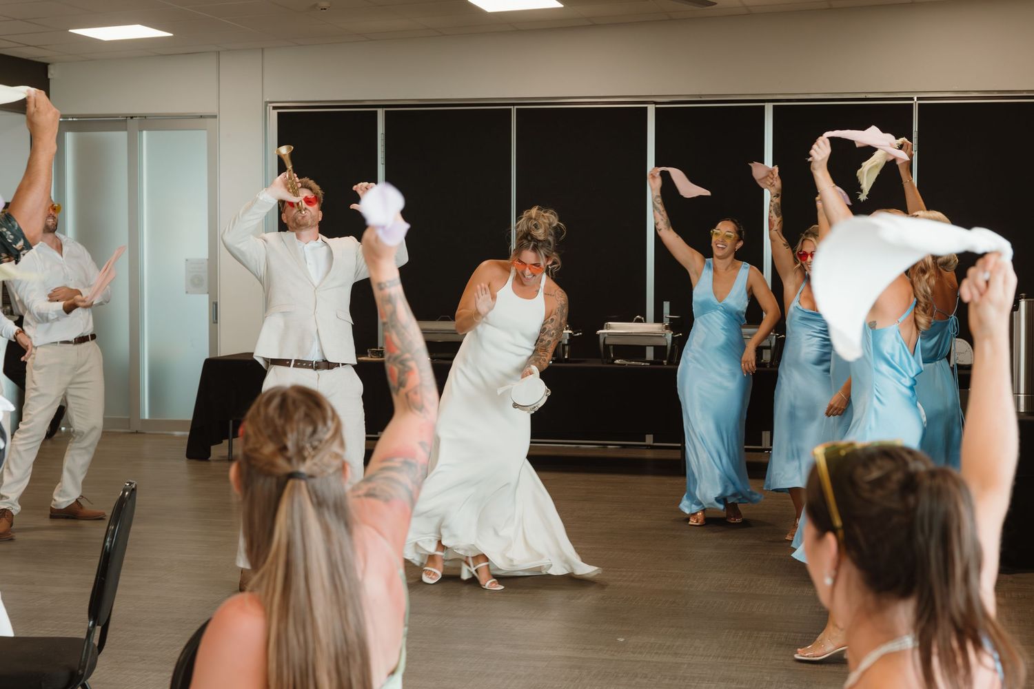 Wedding party dancing with white napkins raised at a lively indoor wedding reception celebration.