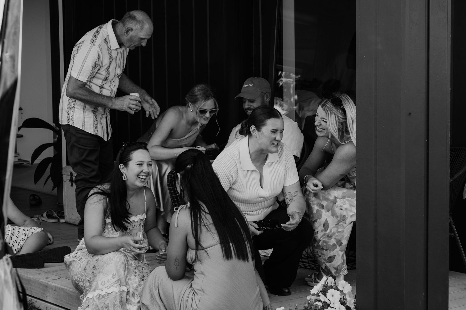Black and white photo of a joyful group of friends laughing and socializing together at a casual outdoor gathering.