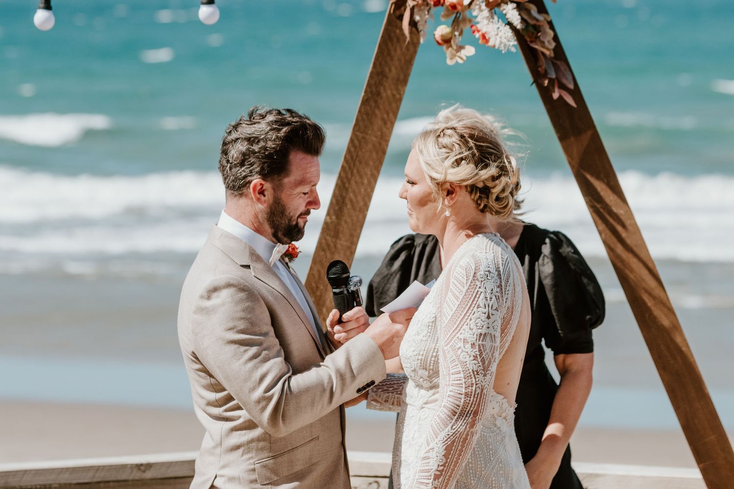 A couple exchanges vows under a wooden arch during their intimate beach wedding ceremony.