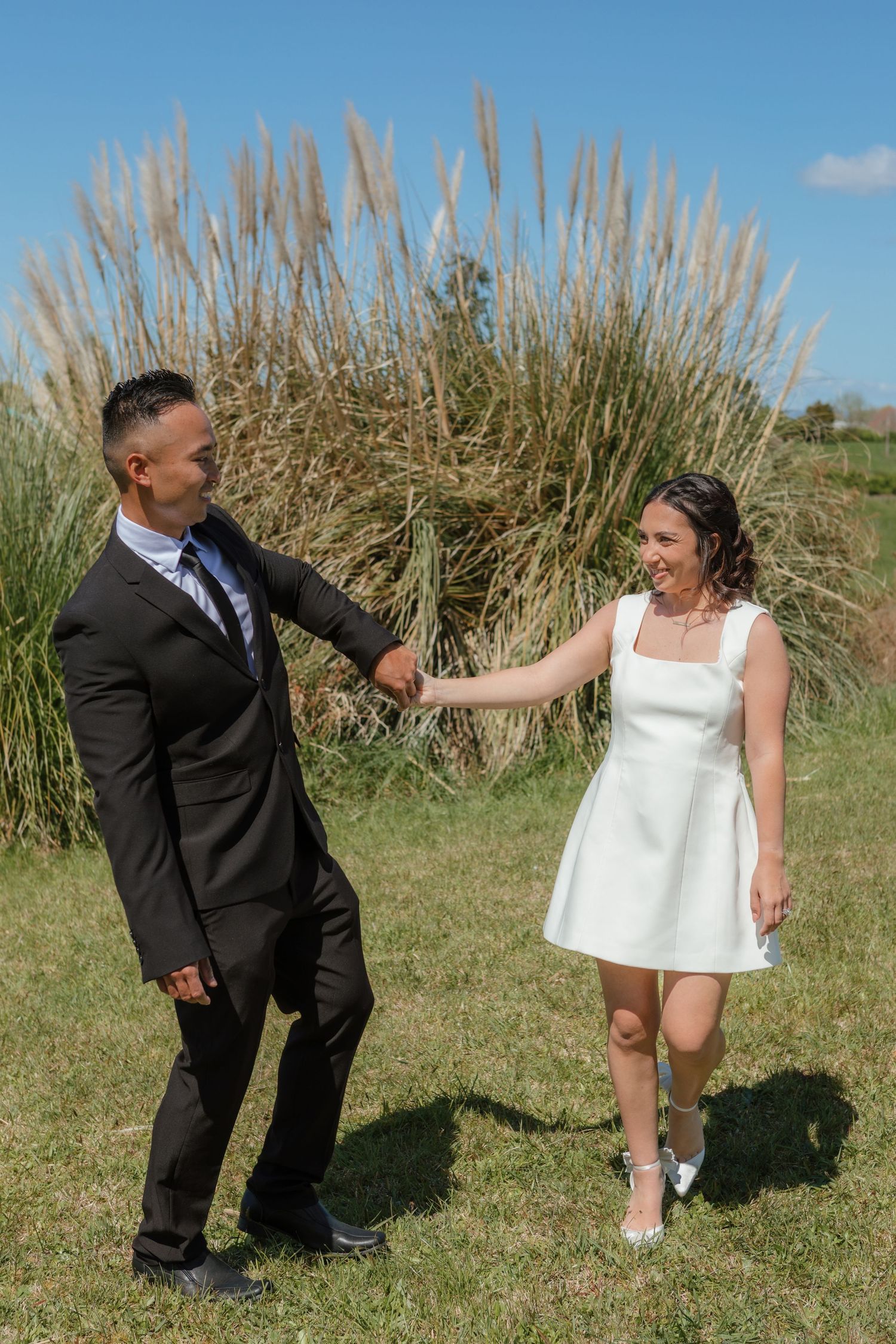 Couple dancing playfully on grass with pampas grass in the background.