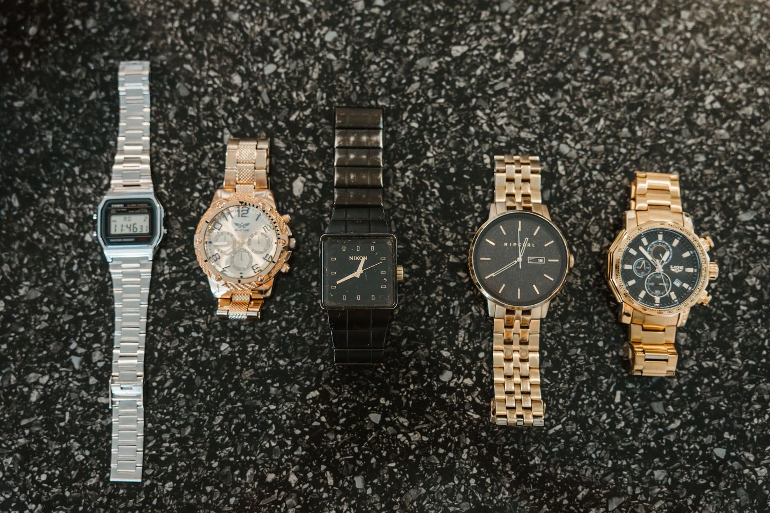 A collection of luxury watches with various metal bands and faces arranged in a row against a dark background.