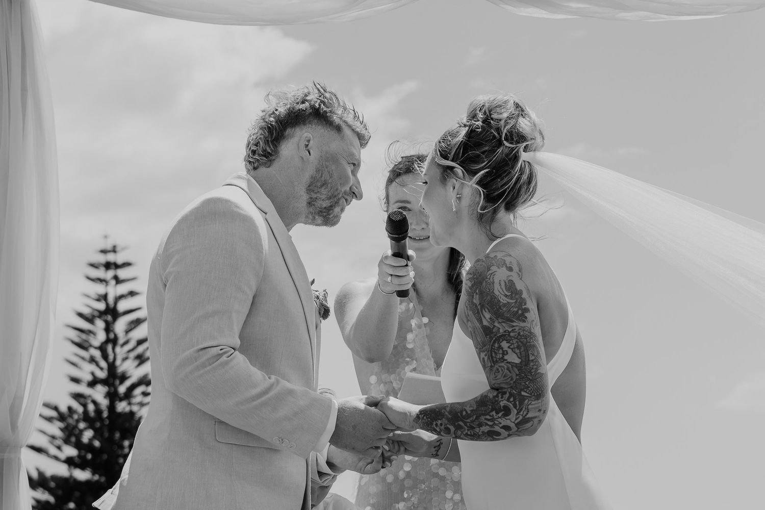 Black and white photo of a bride and groom laughing during wedding vows ceremony outdoors.