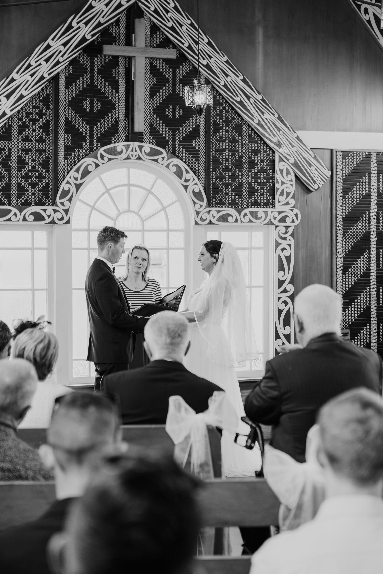 A traditional church wedding ceremony takes place in a chapel with ornate wooden carvings and a decorative cross above the altar.