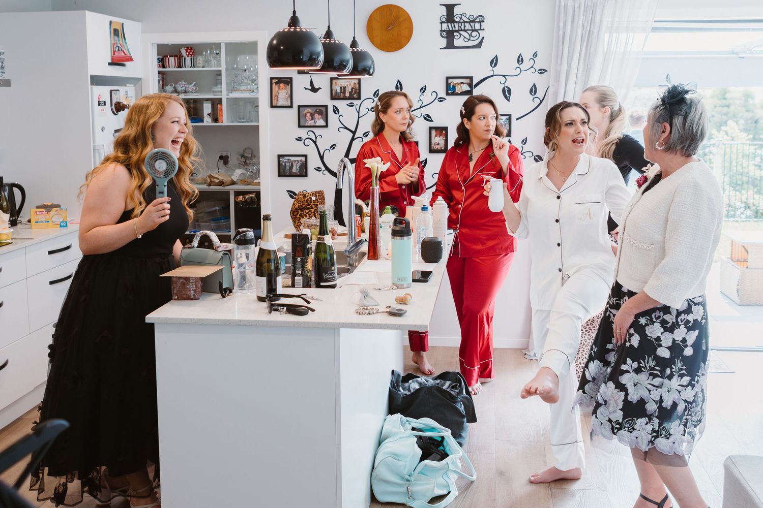 A festive group in formal attire enjoys drinks and conversation in a modern white kitchen with pendant lighting.