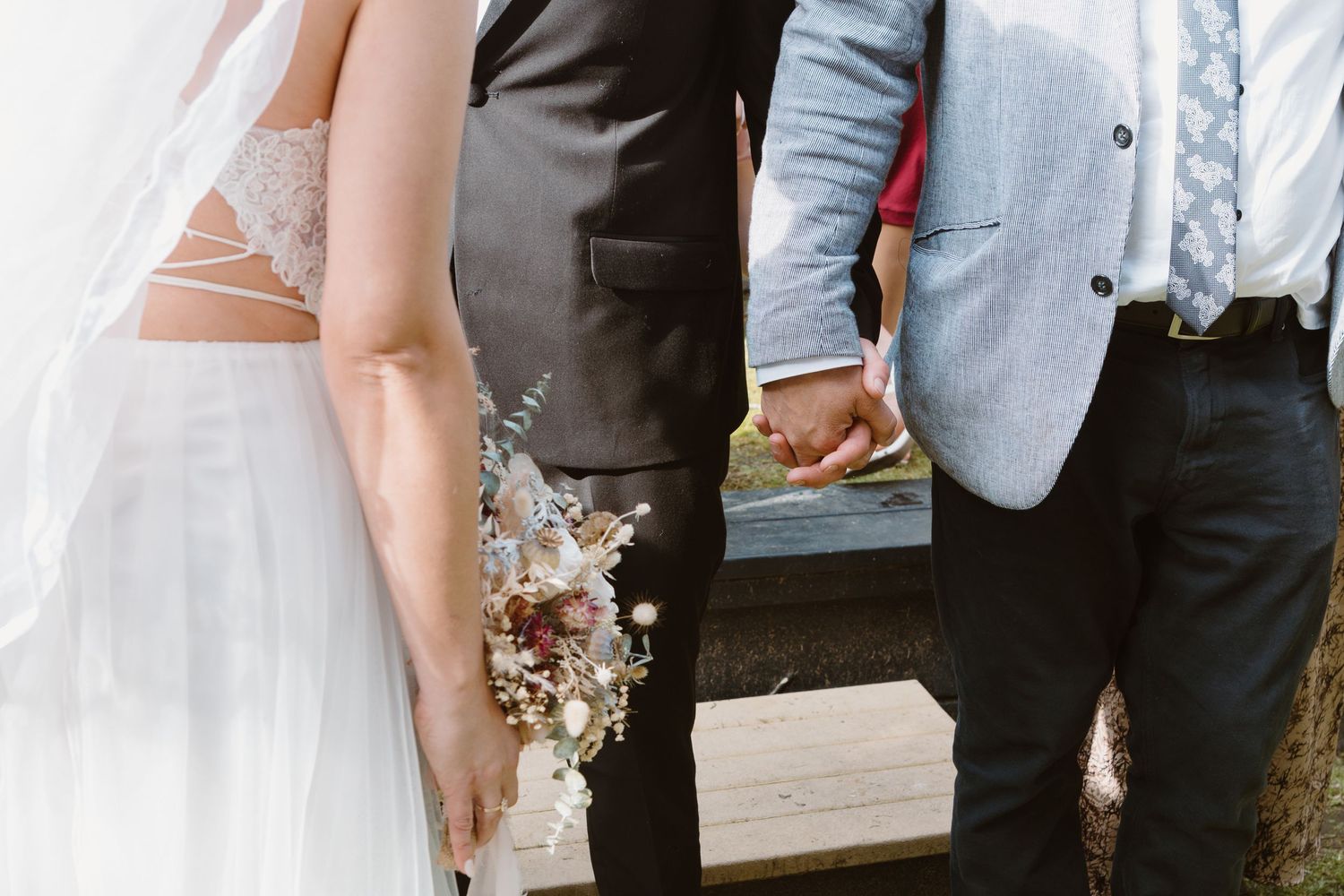 Close-up detail shot of wedding attire and bouquet during outdoor ceremony.