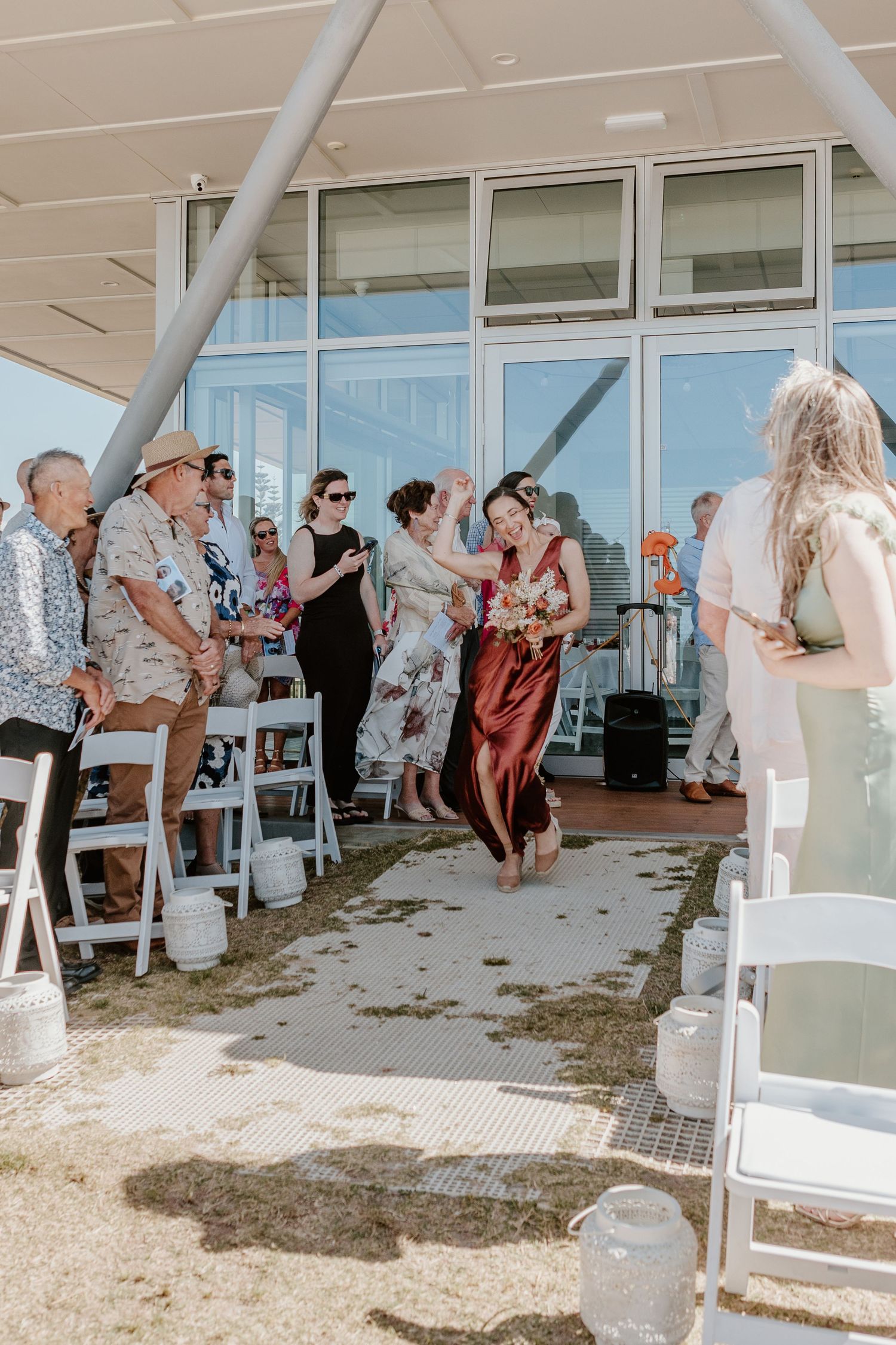 Wedding ceremony guests gather under a white tent structure near glass windows for an outdoor celebration.
