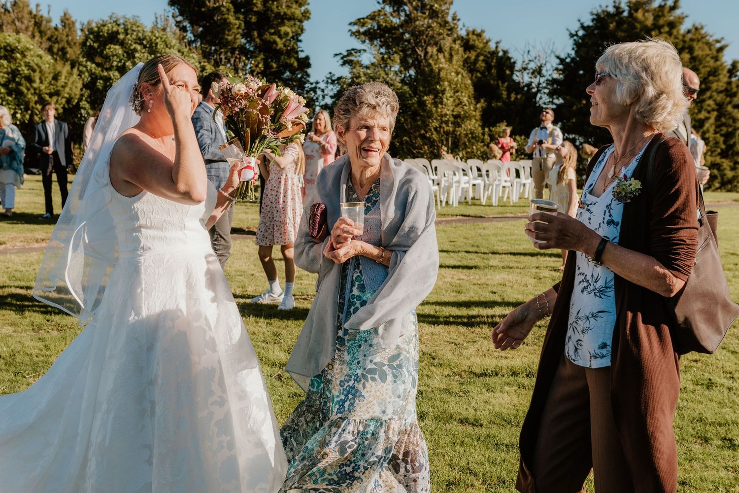 Wedding guests throw colorful eco-friendly confetti on a bright sunny day during an outdoor celebration.