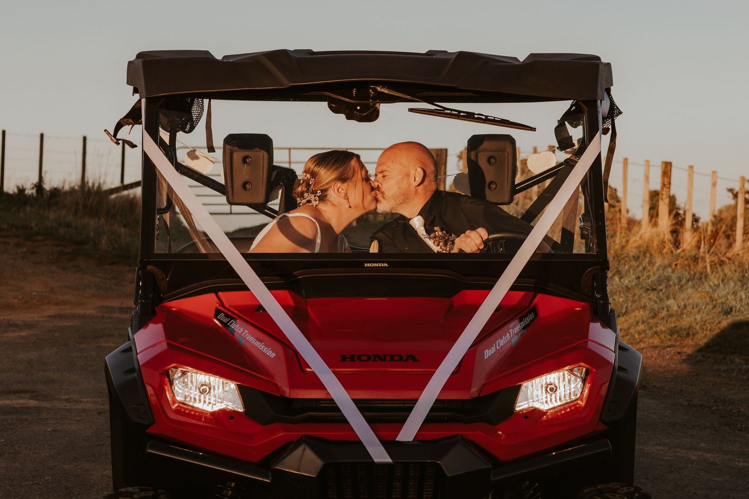Red utility vehicle decorated with white ribbons captured at sunset with passengers inside.
