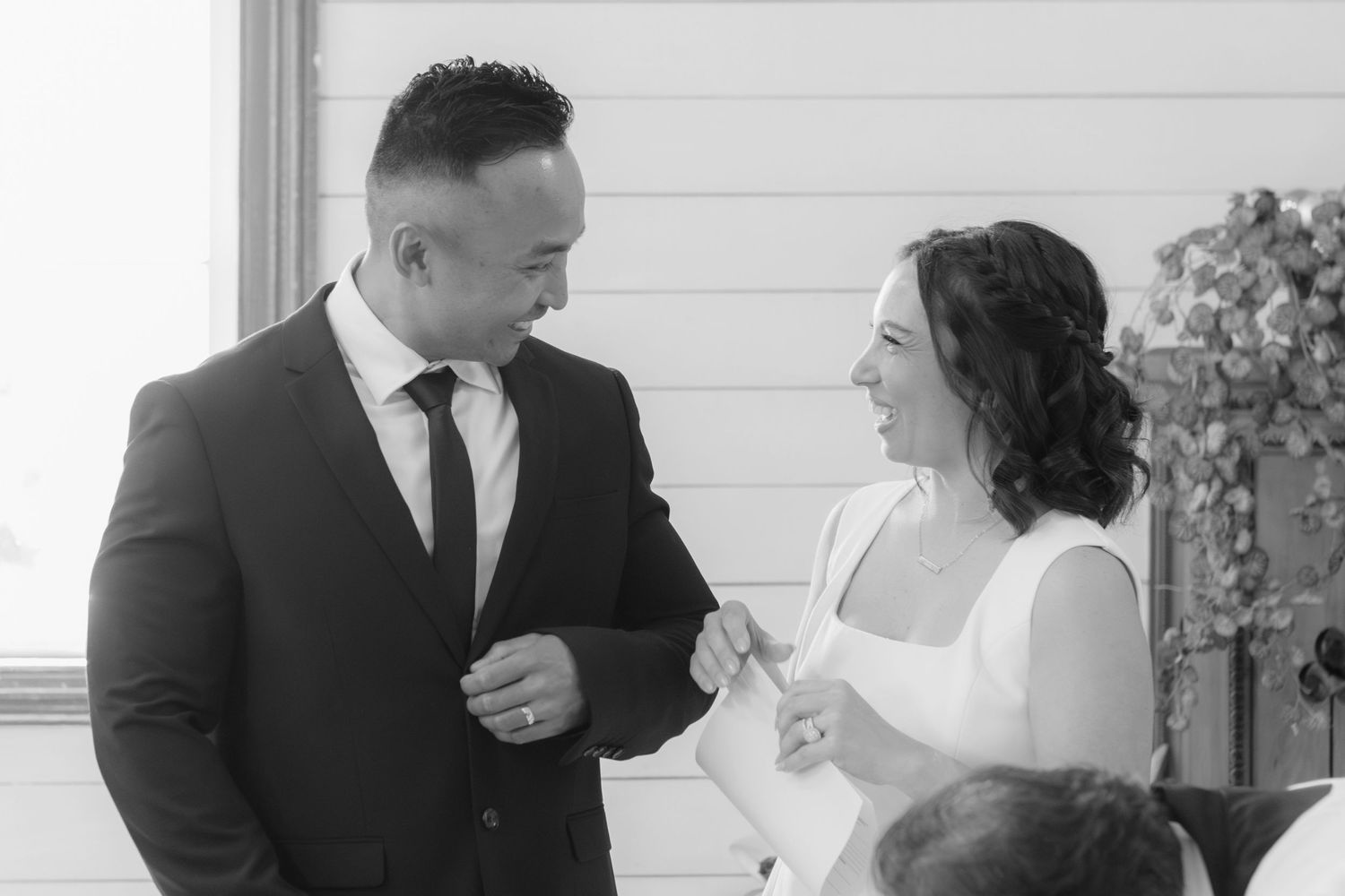 A black and white photo of a couple sharing a happy moment in formal attire during a wedding celebration.
