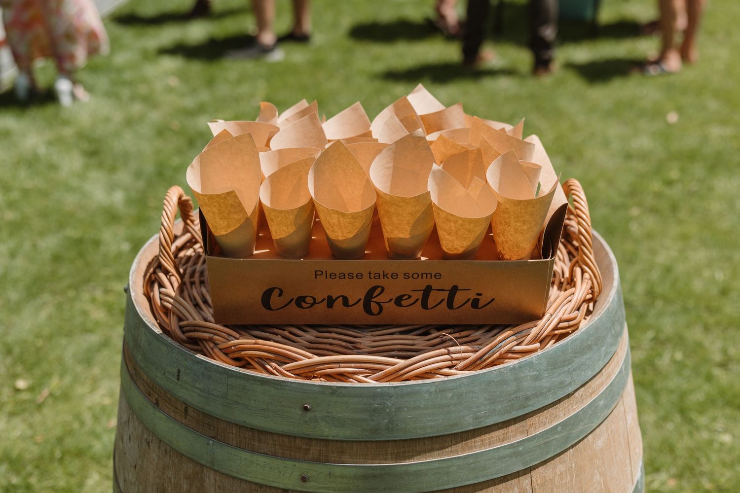Rustic wedding confetti cones displayed in a wooden box on a barrel, perfect for an outdoor ceremony.