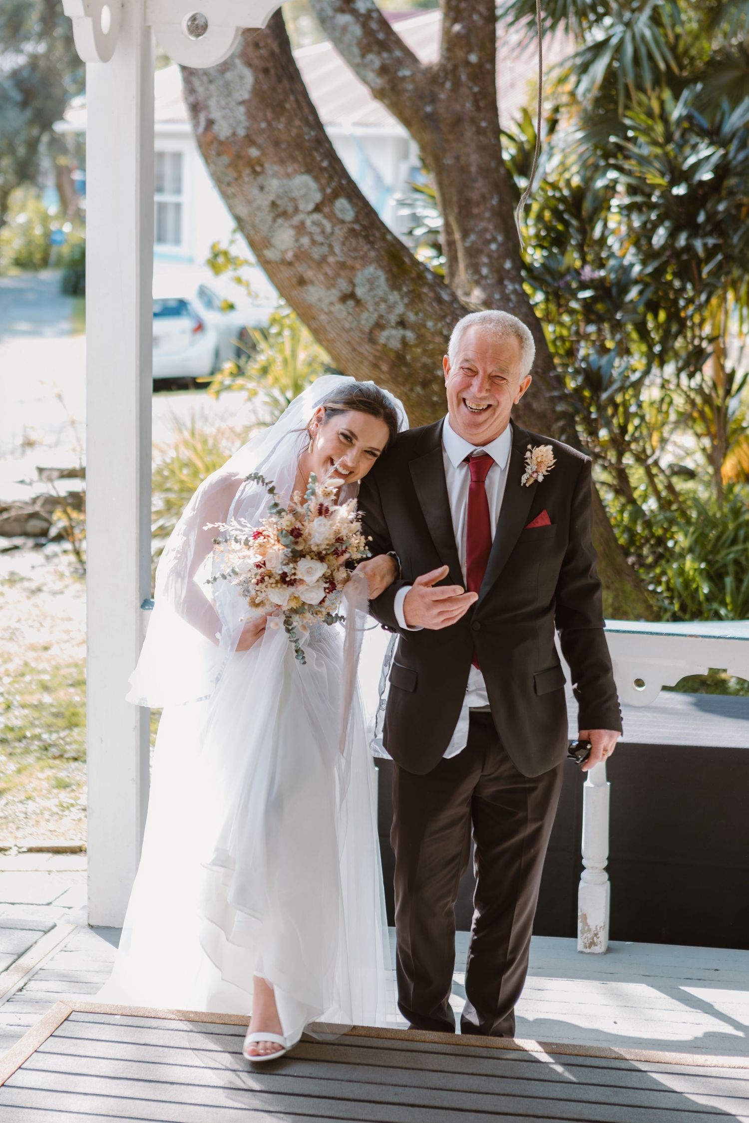 A wedding scene on a covered porch with someone in a white dress holding a bouquet and someone in formal attire.